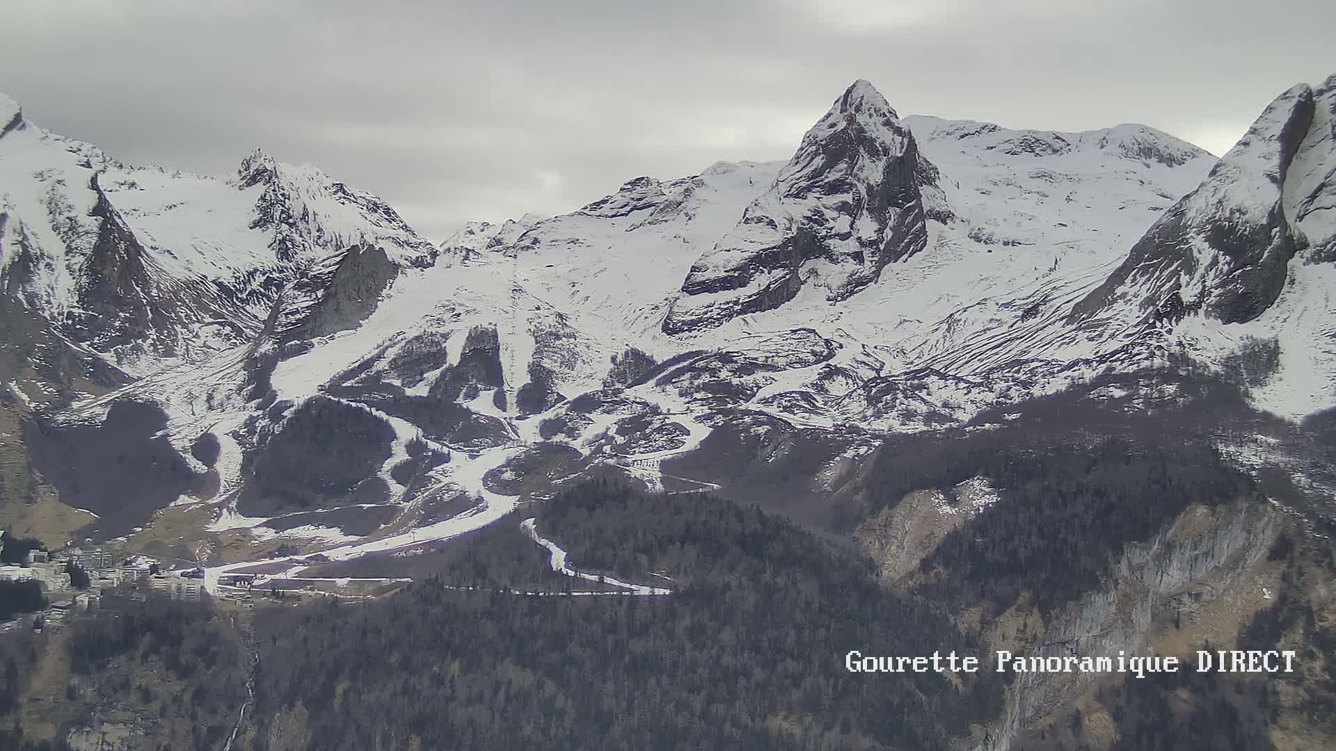 A snow-covered mountain range with a small village at its base under an overcast sky.