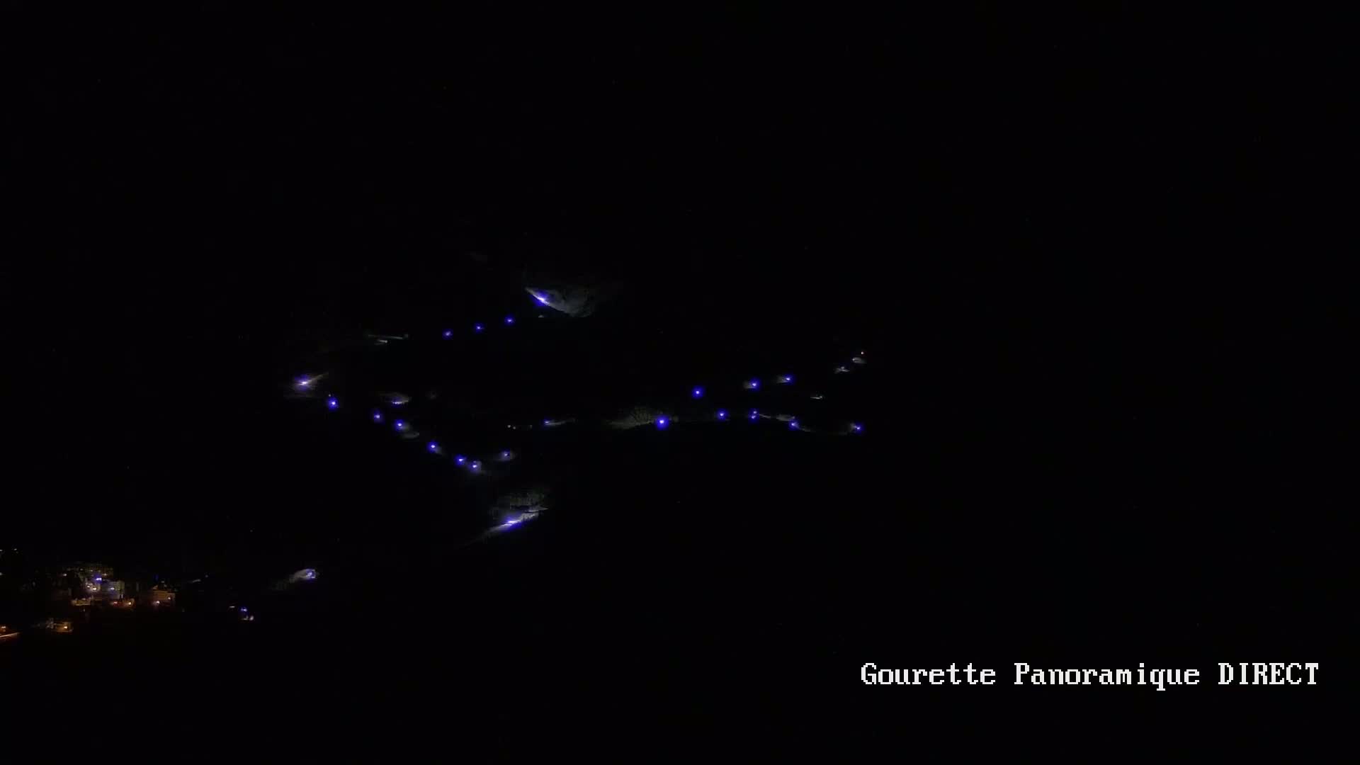 A nighttime long-range view shows a series of small, faint purple lights scattered across a dark hillside.