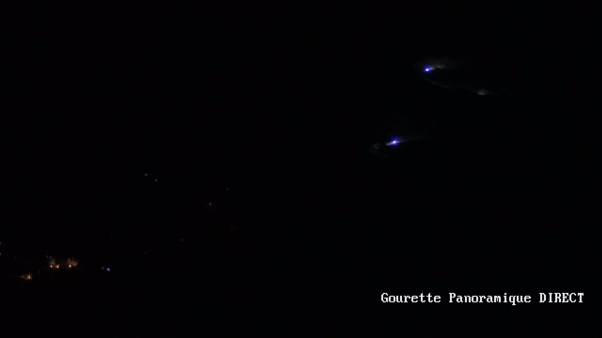 Three faint, bluish lights streak across a dark night sky above a dimly lit landscape.