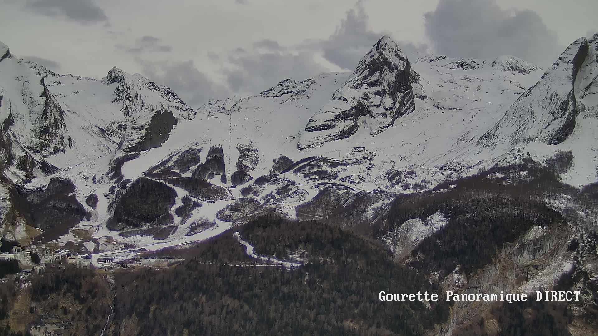 A snow-covered mountain range with a village nestled in the valley below under an overcast sky.