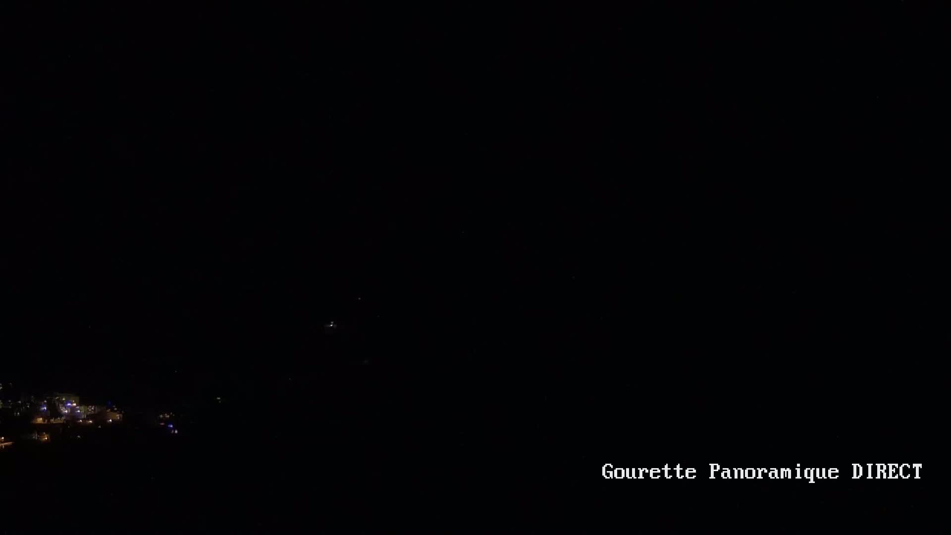 A nighttime view shows a small cluster of distant lights at the bottom of a dark scene.