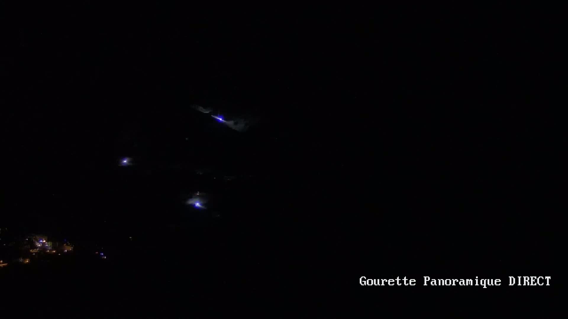 A nighttime, dark landscape shows several streaks of lightning illuminating a distant town below.