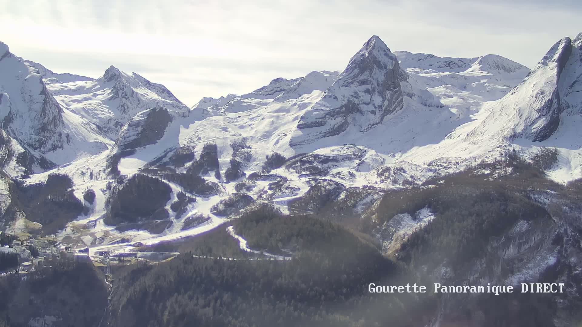 A snow-covered mountain range with ski slopes and a village nestled below, under a bright, sunny sky.