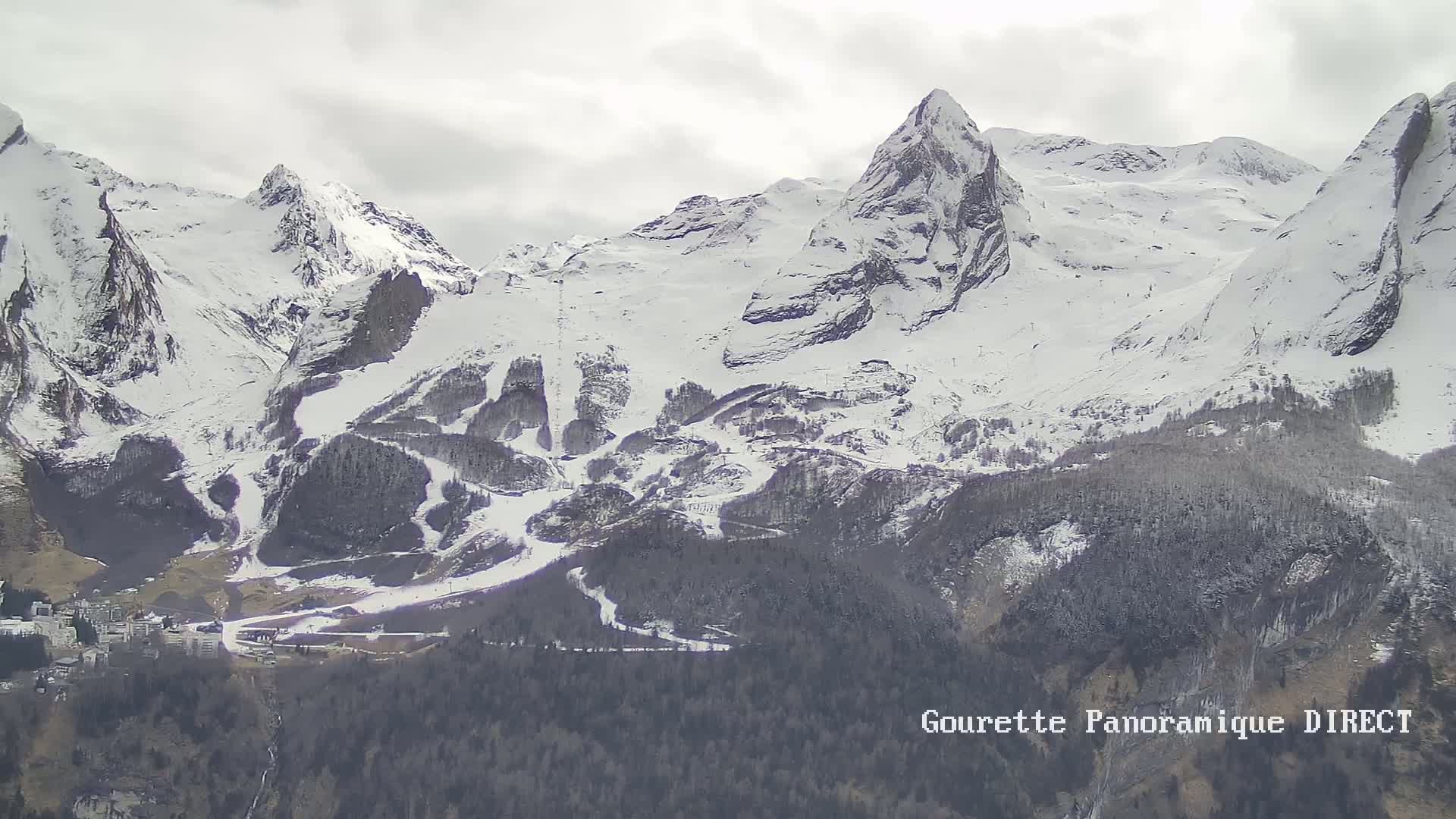Snow-covered mountains with ski slopes and a town nestled at their base under an overcast sky.