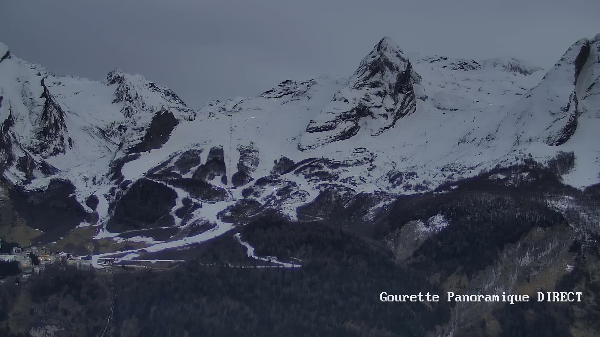 A snow-covered mountain range with ski runs, under a cloudy, dusky sky.