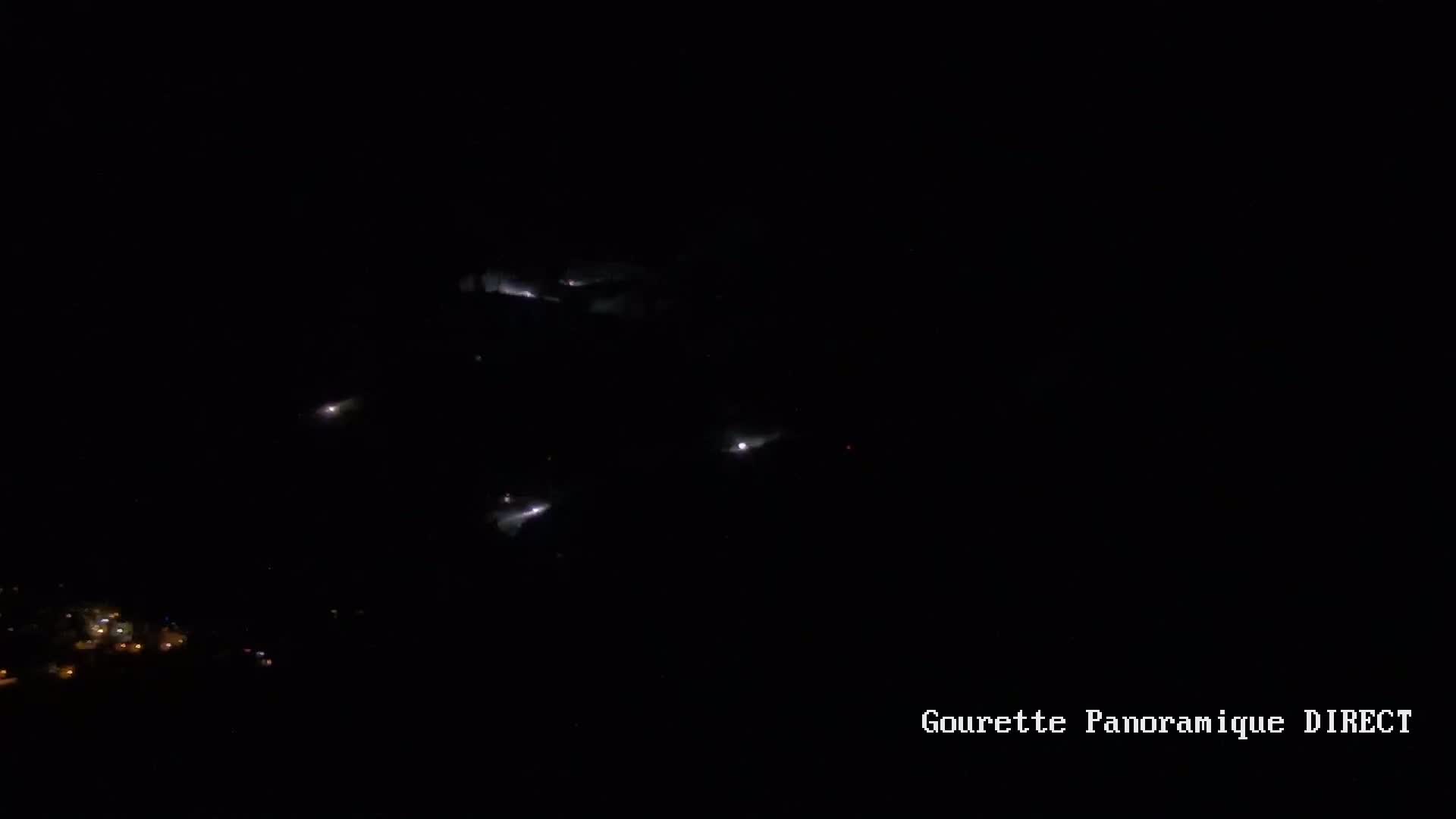 A nighttime, high-angle view shows several faint lights scattered across a dark landscape.