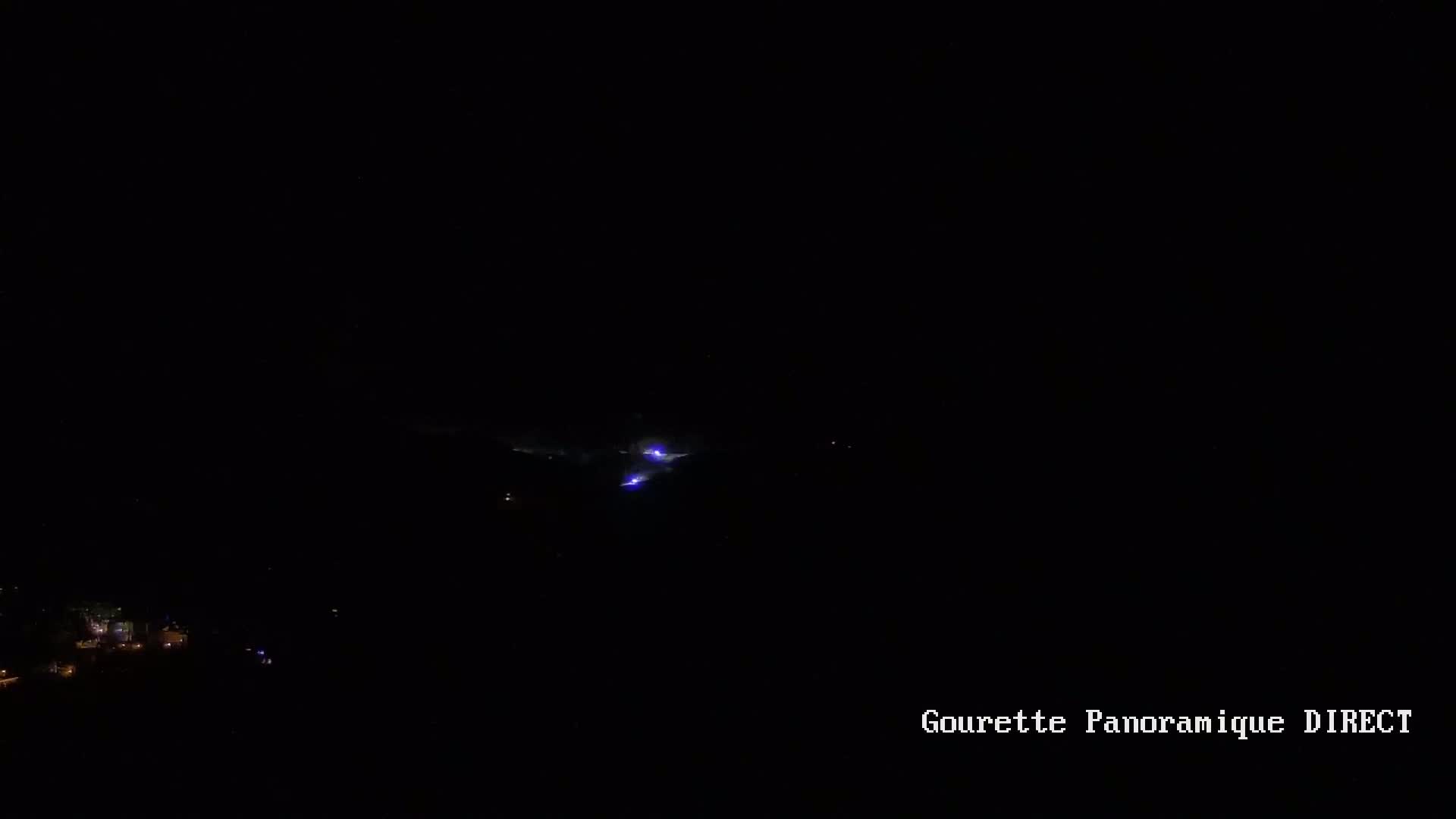 A nighttime long shot shows faint purple lightning strikes in a dark, mountainous area with a few small lights visible in the distance.