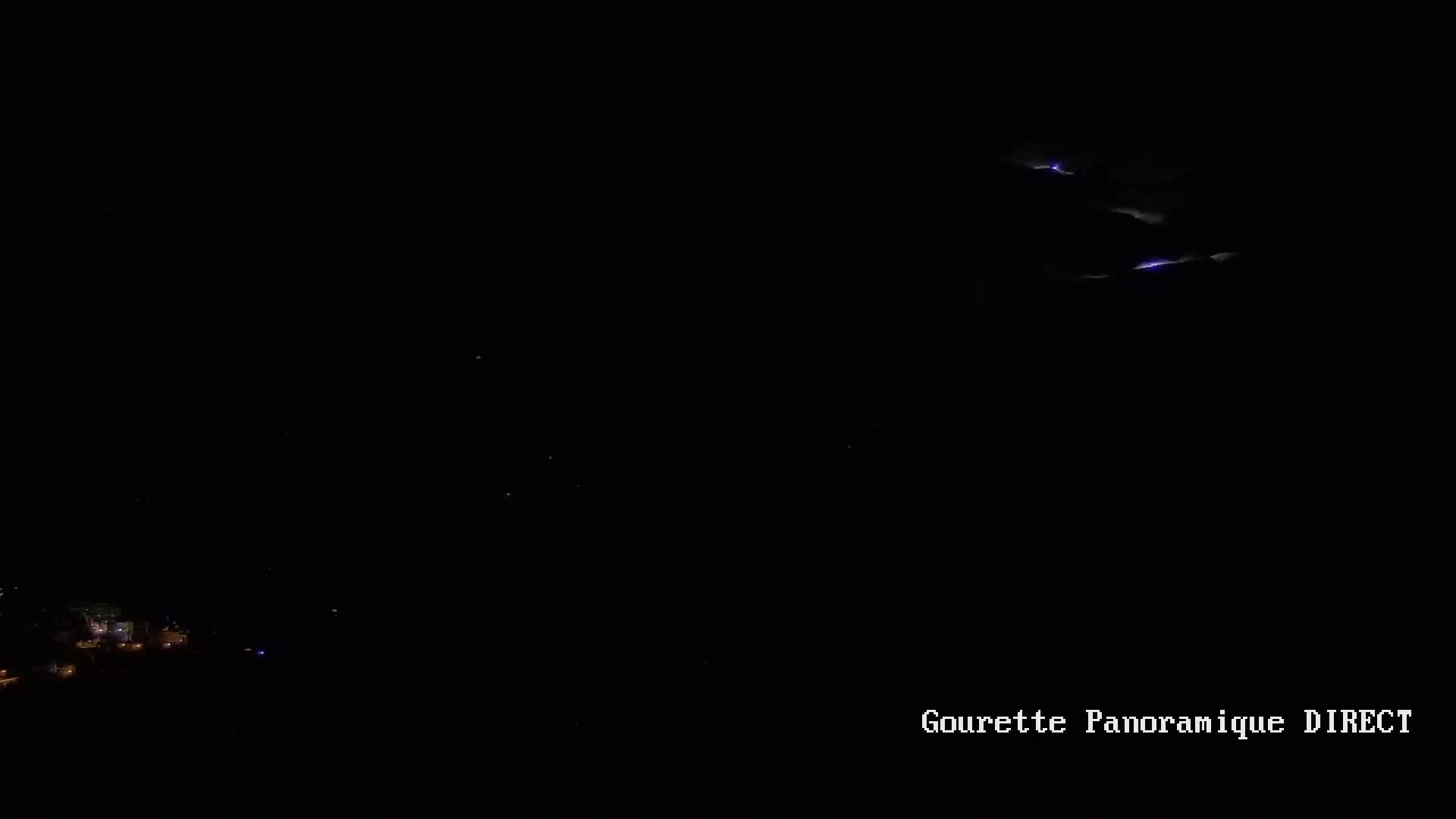 A nighttime long shot shows a few distant lightning strikes above a dark landscape with some faint lights visible below.