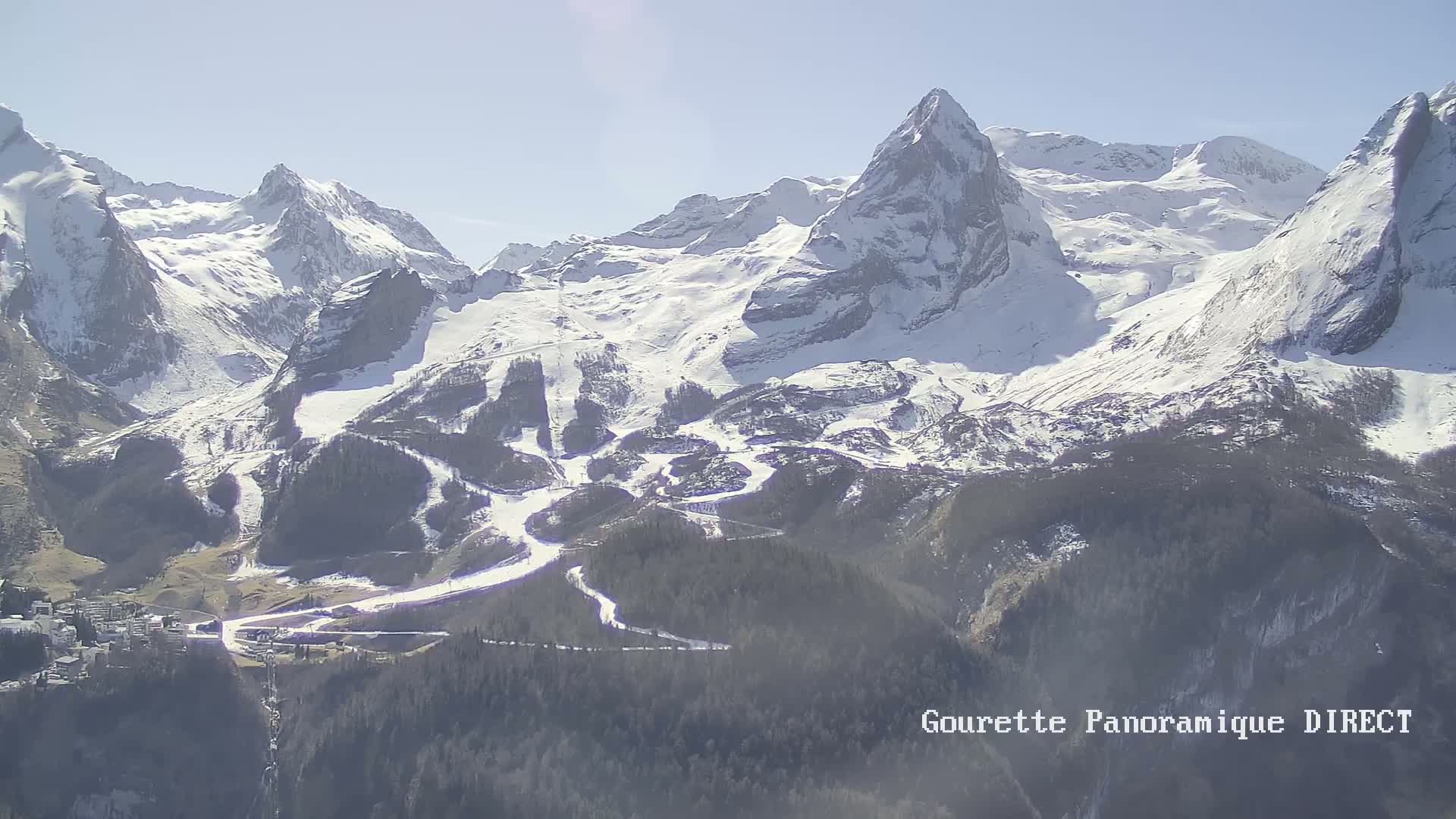 A snow-covered mountain range with ski runs is visible under a bright, sunny sky.
