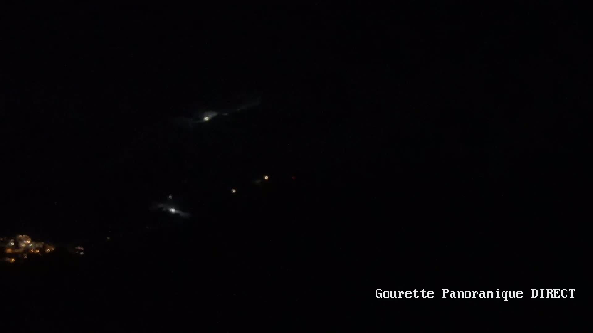 A nighttime long shot shows faintly lit clouds and distant lights on the ground, possibly a town, under a dark sky.