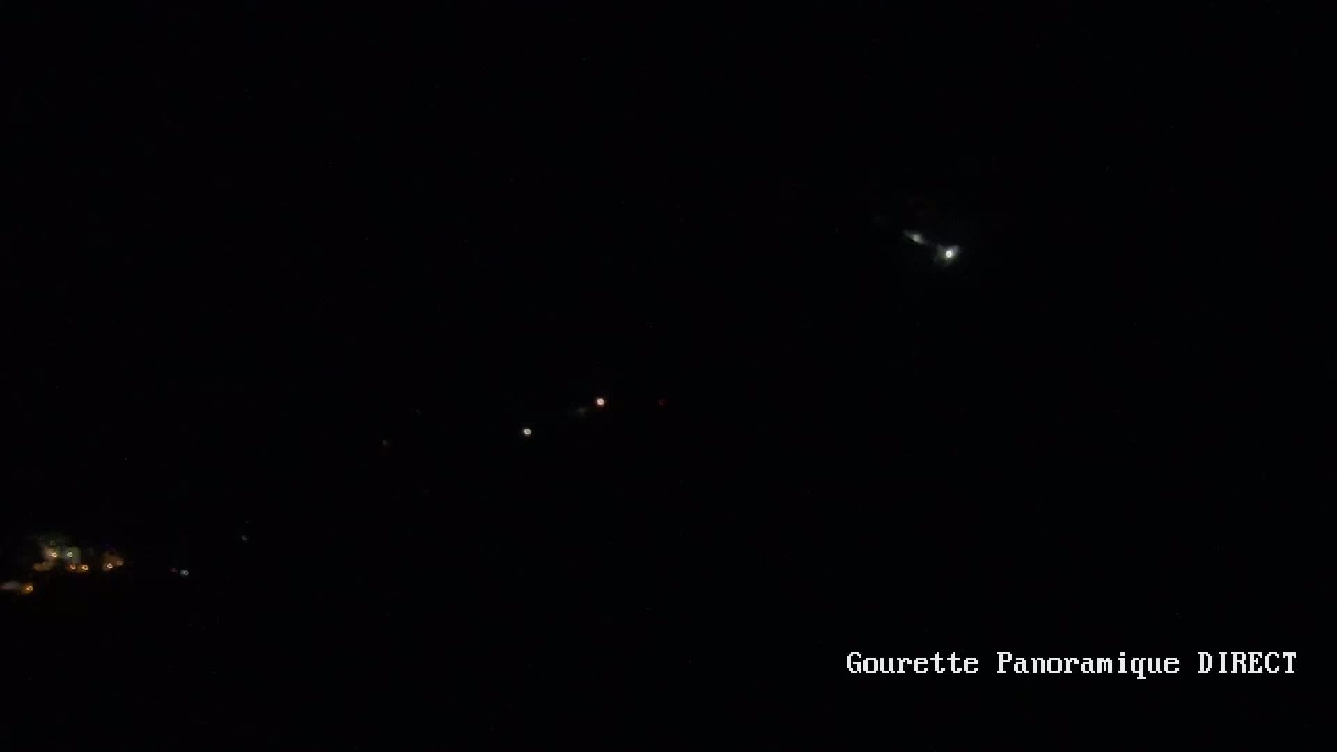 A nighttime, long-range shot shows a bright light, possibly the moon, and several fainter lights, possibly stars or distant lights on the ground, in a dark sky.