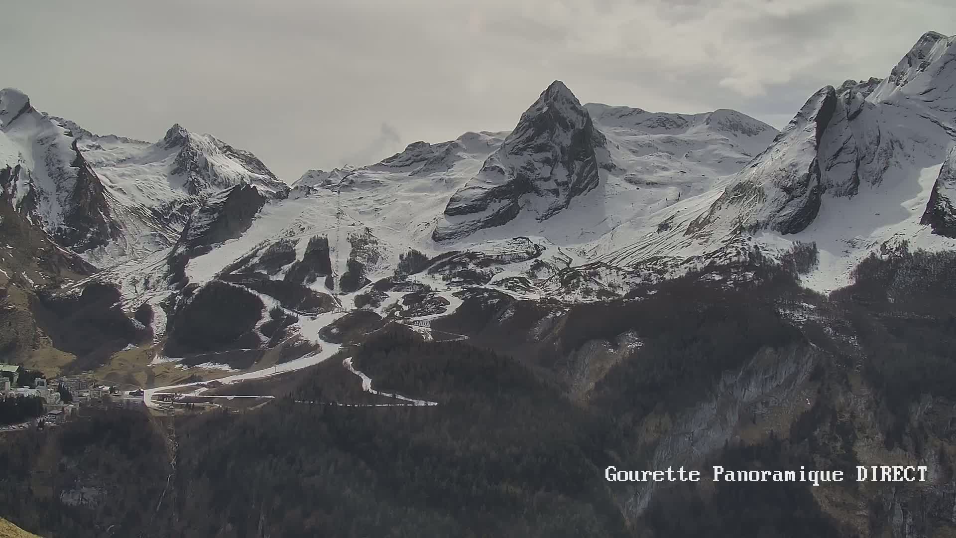A long-range view shows a snow-covered mountain range with ski runs visible on its slopes under an overcast sky.