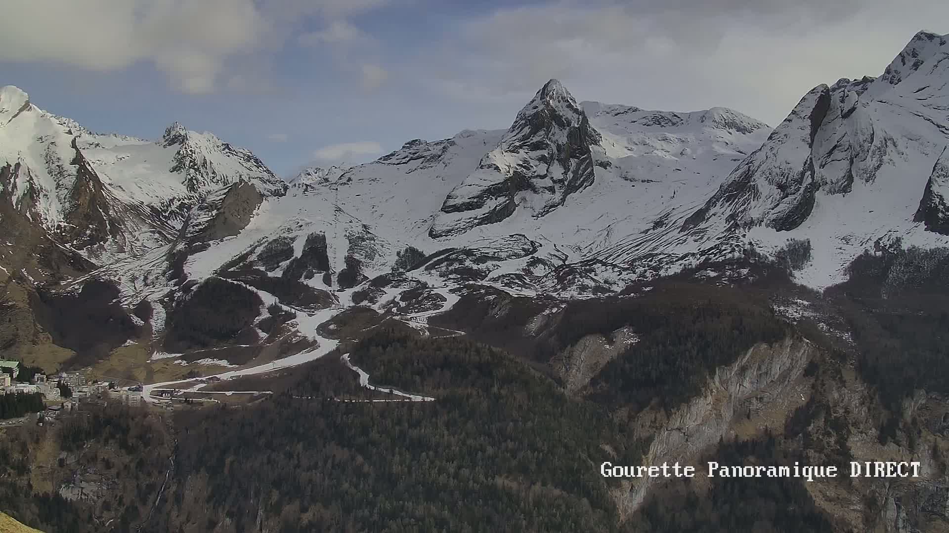 A snow-capped mountain range, partially cloudy, with a village nestled in the valley below.