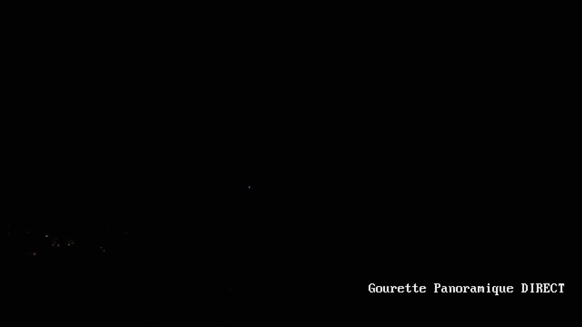A nighttime, long-range view shows a scattering of faint lights in the distance below a very dark sky.