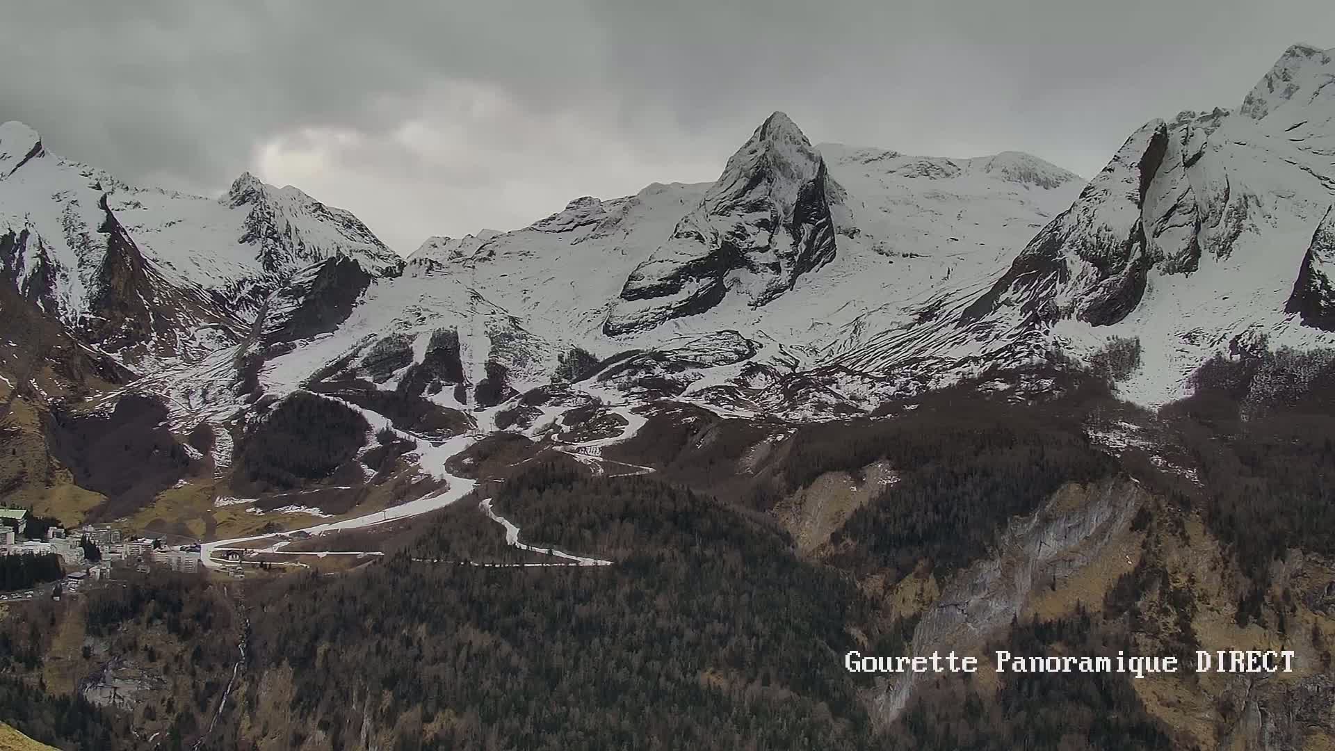 A snow-capped mountain range with a small village at its base under an overcast sky.