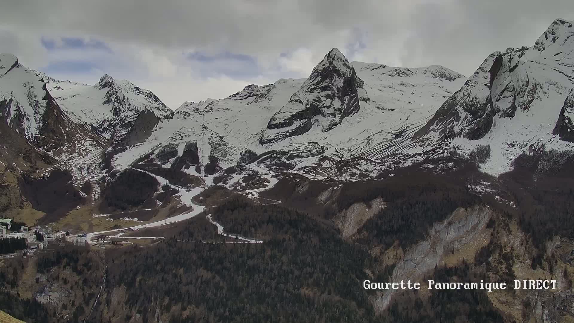 A snow-covered mountain range with a small village nestled in the valley below, under a cloudy sky.
