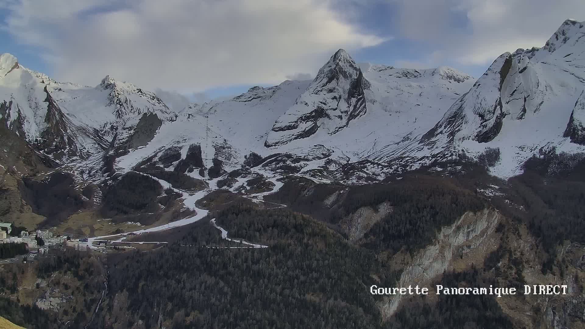 A snow-covered mountain range with a town nestled in the valley below, under a partly cloudy sky.