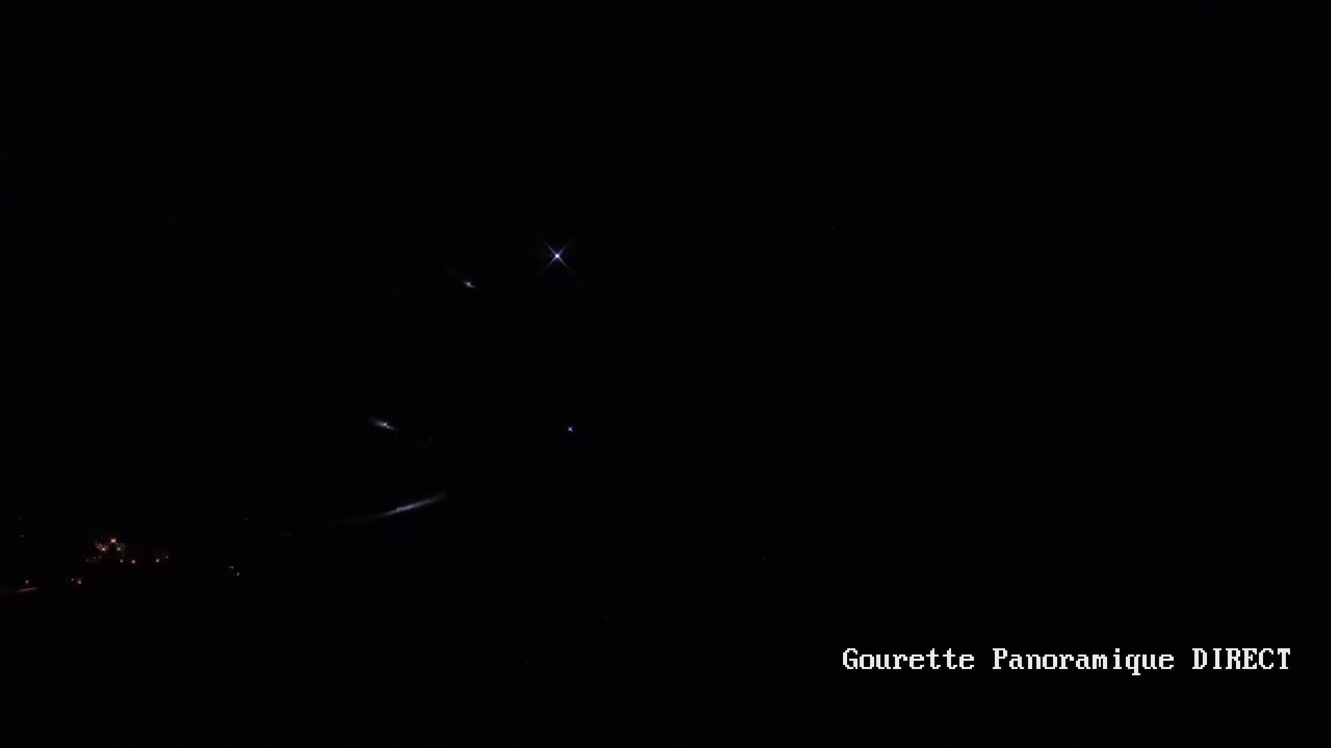 A dark nighttime scene shows faint lights in the distance and a few bright lights in the dark sky.