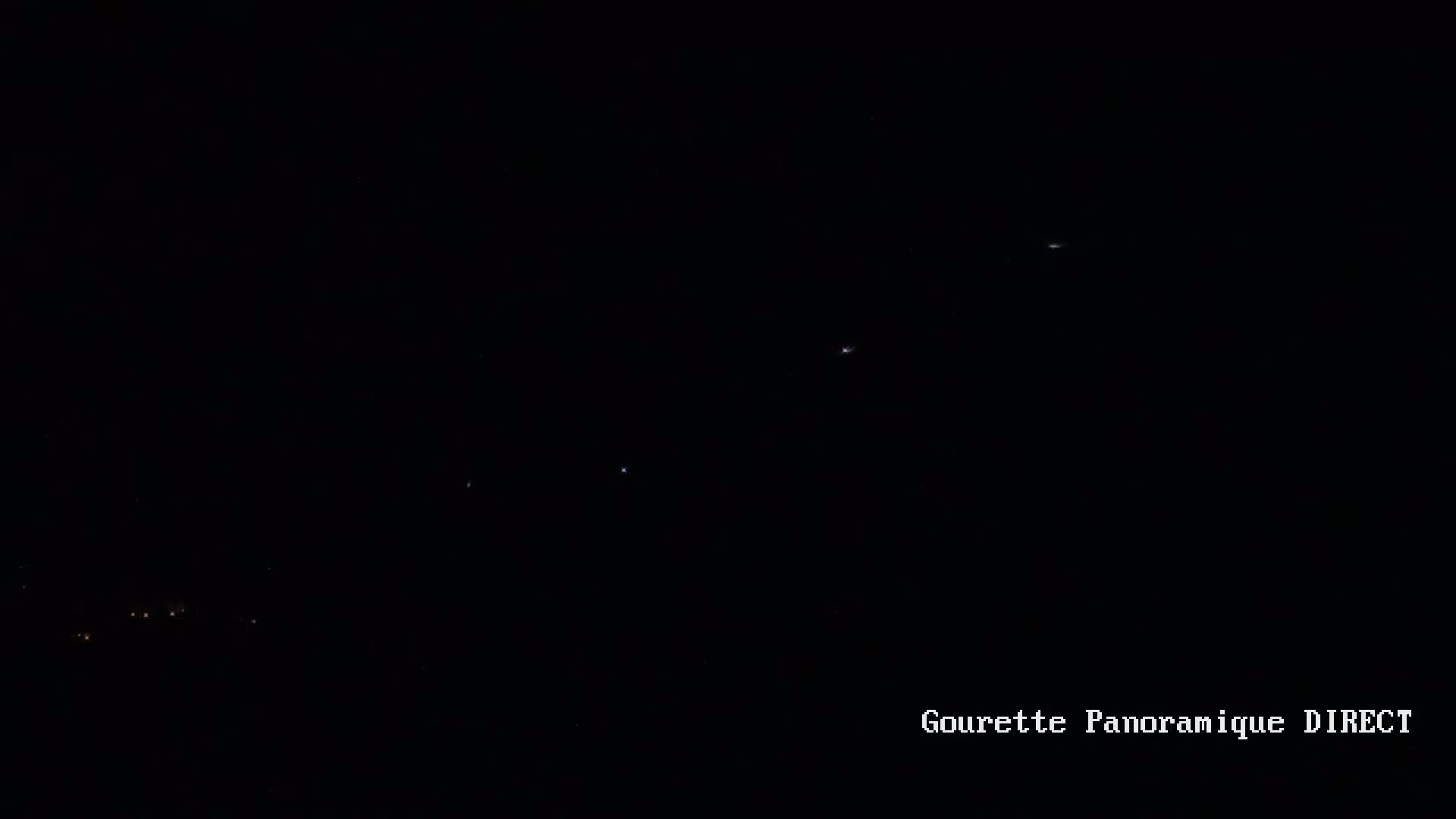 A nighttime, dark sky shows a few faint lights in the distance and some very small, distant lights possibly stars or aircraft.