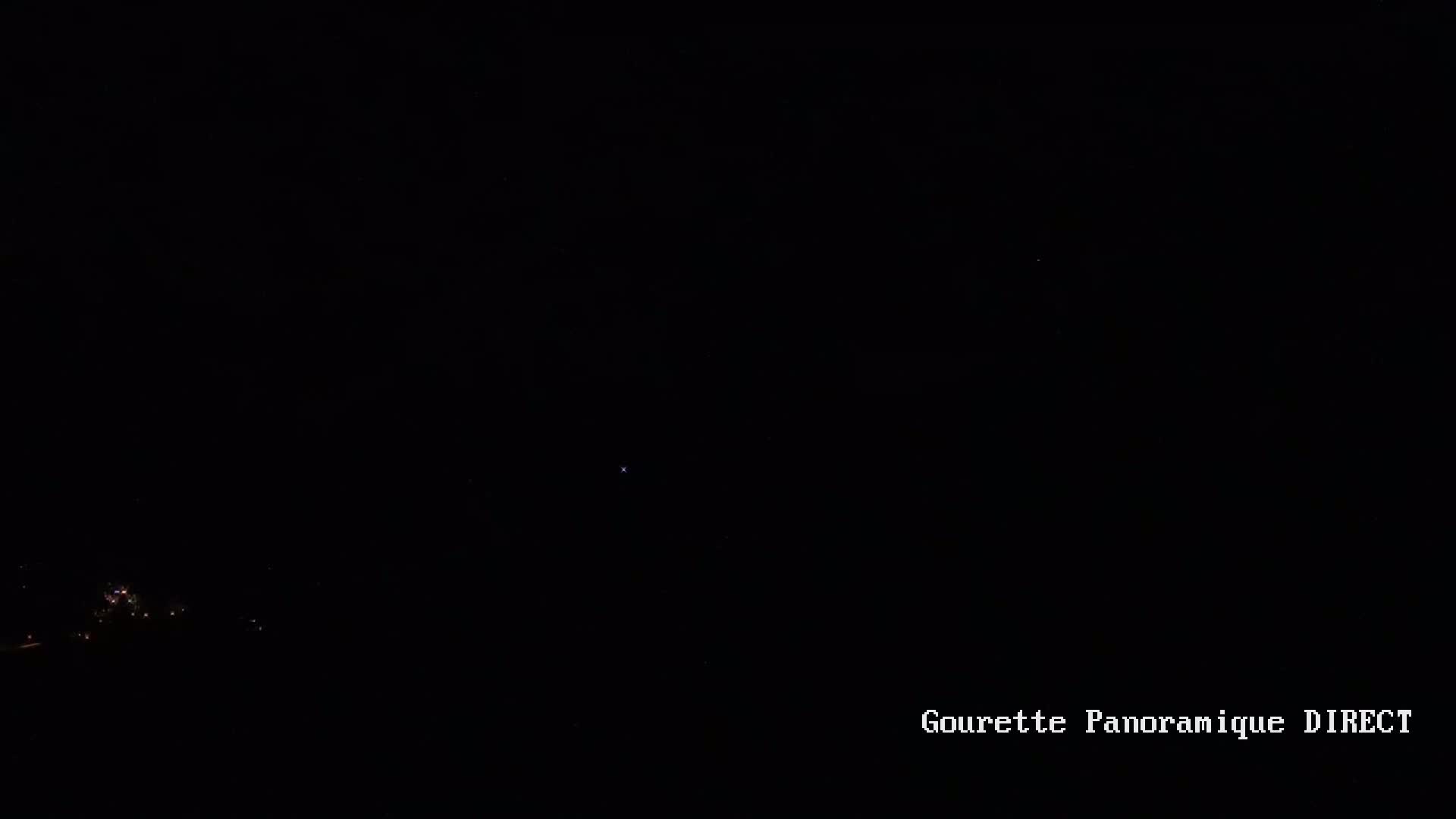 A nighttime, long shot of a few small lights in the distance under a dark, clear sky.