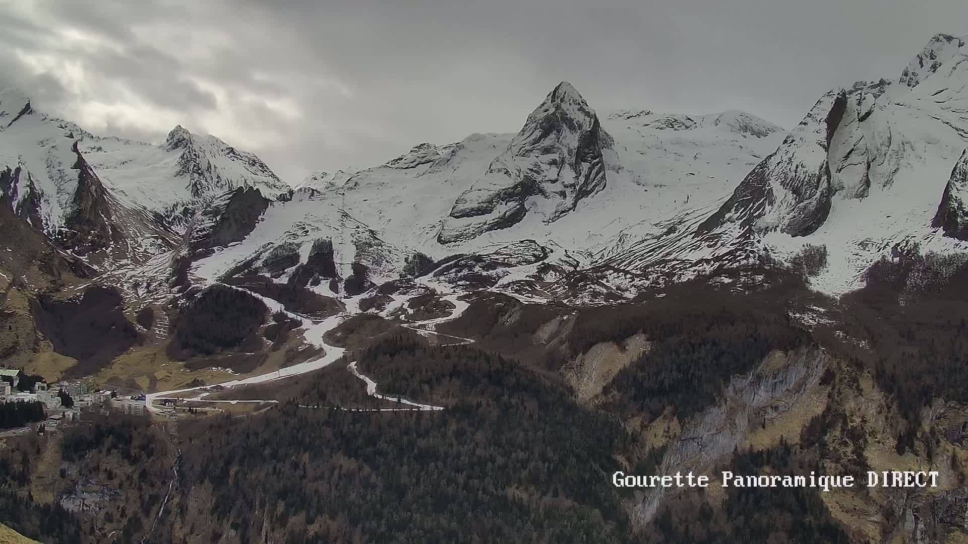 A snow-covered mountain range with a valley below, under a cloudy sky.