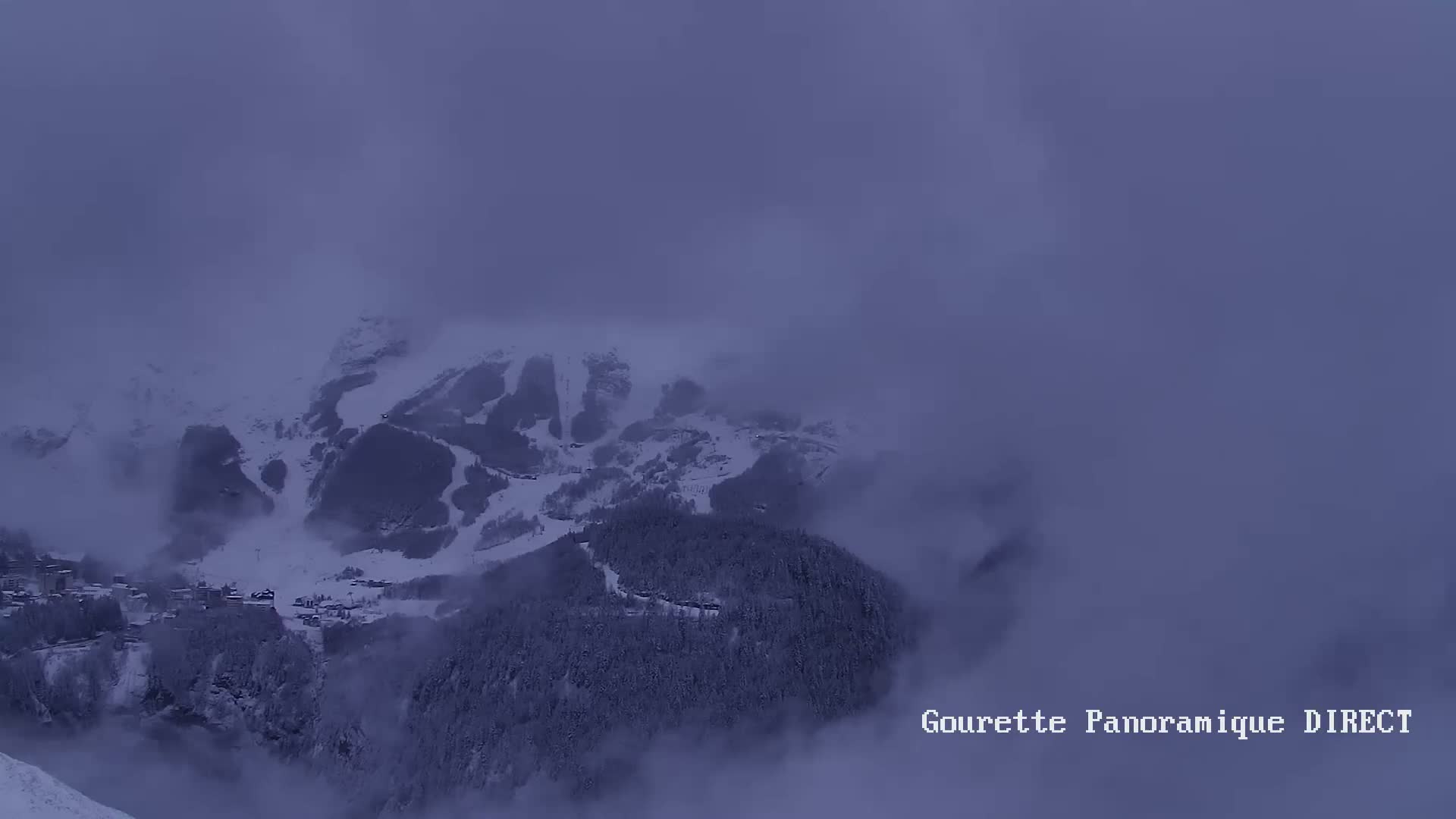 A snow-covered mountain range is partially obscured by a thick fog under a dark, overcast sky.