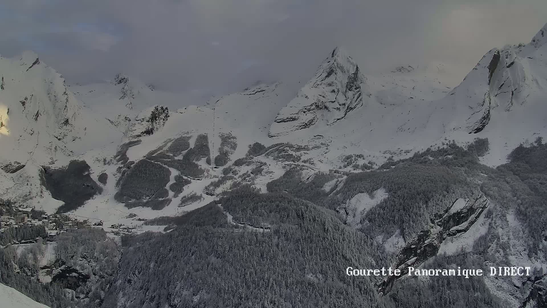 A snow-covered mountain range with a village nestled in the valley below, under an overcast sky.