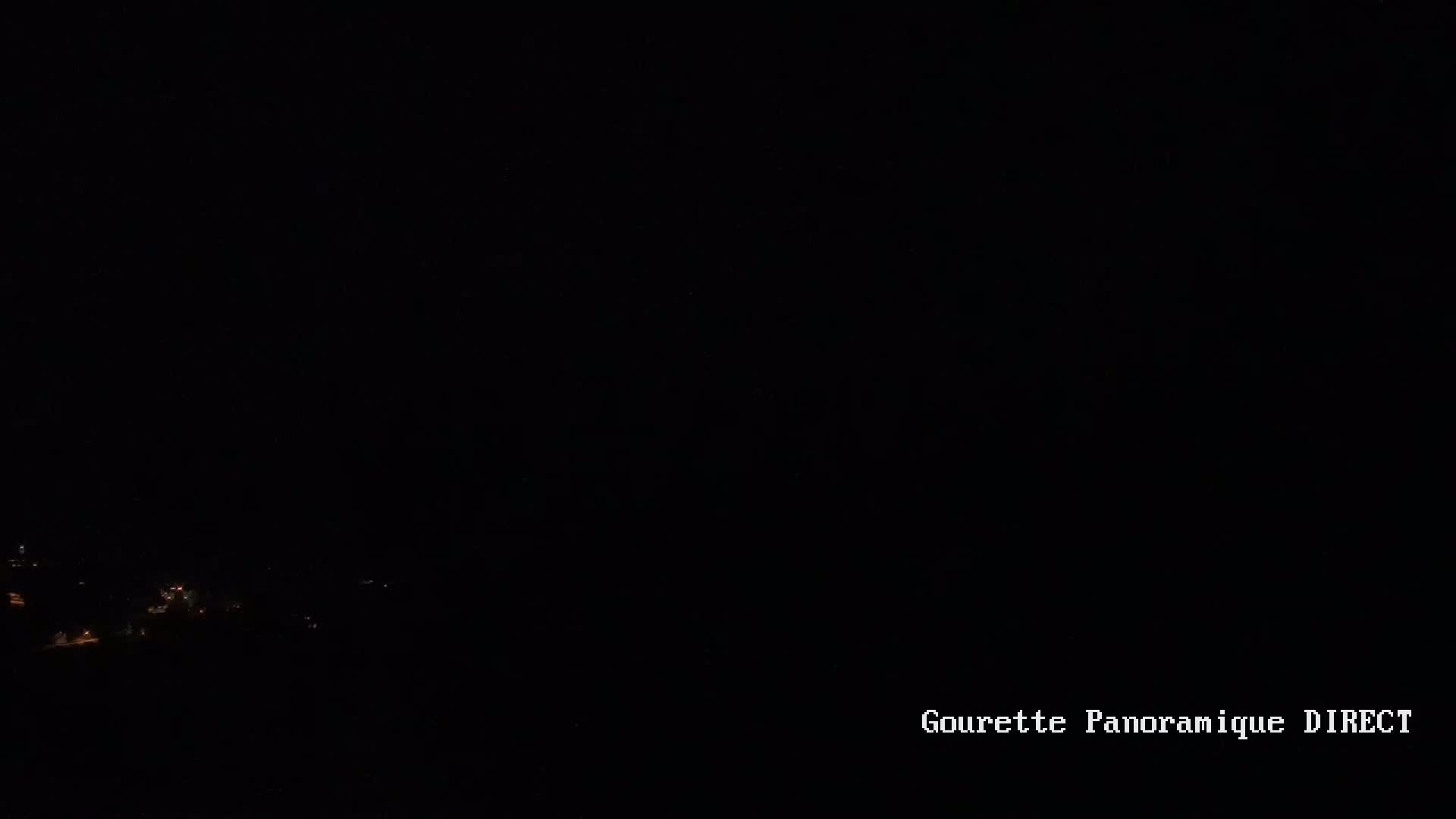 A dark, nighttime view of dimly lit houses or buildings in a valley.