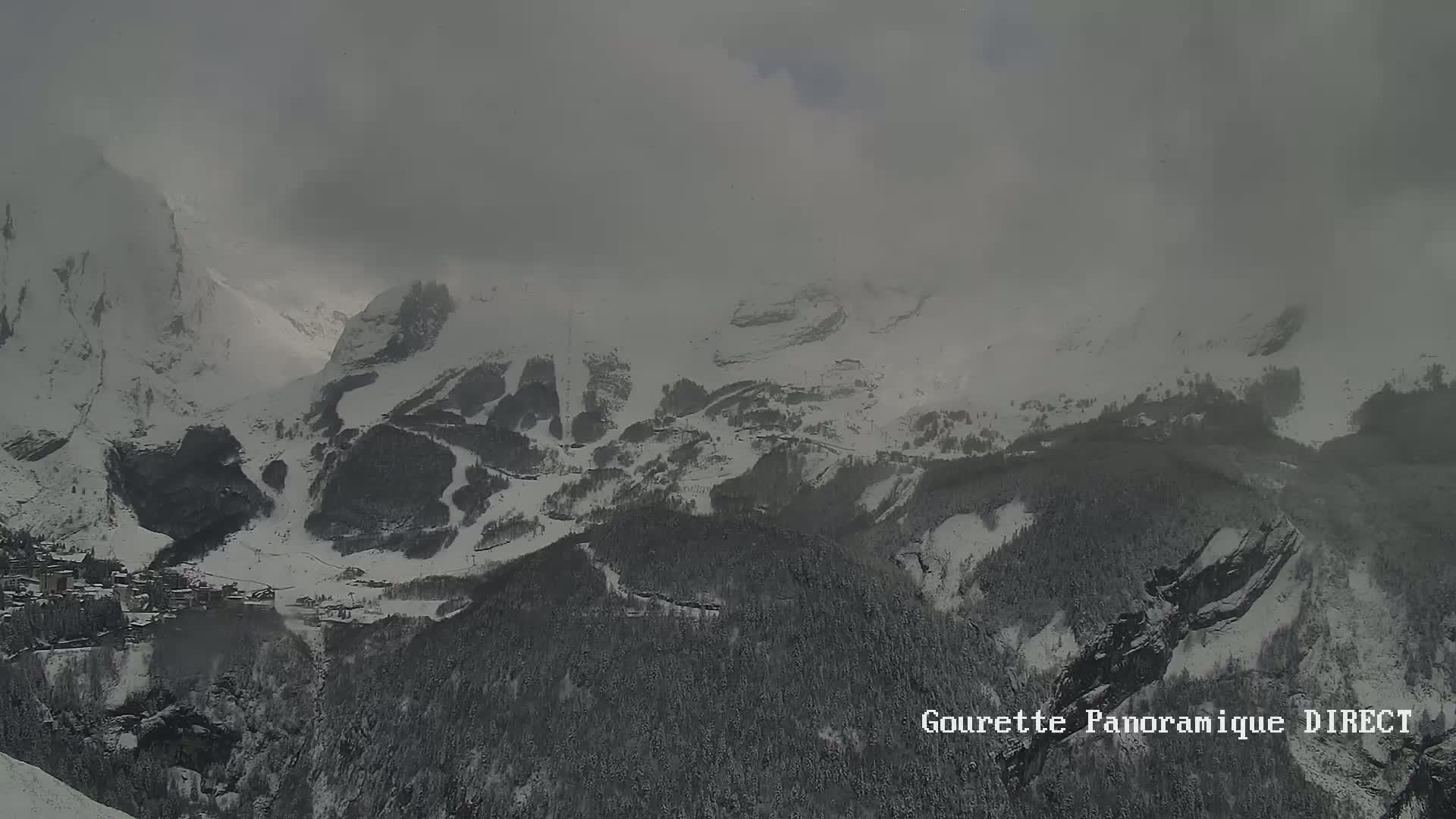 A snow-covered mountain valley is partially obscured by heavy clouds.