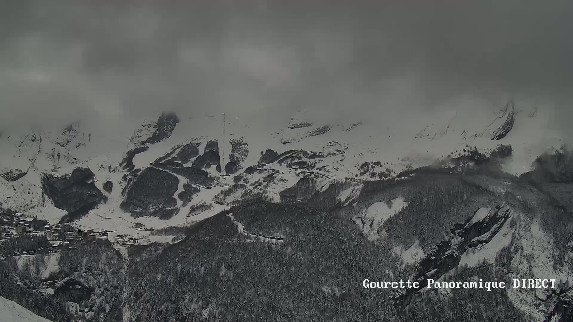 A snow-covered mountain range is shrouded in a thick fog, with a small village nestled in the valley below.