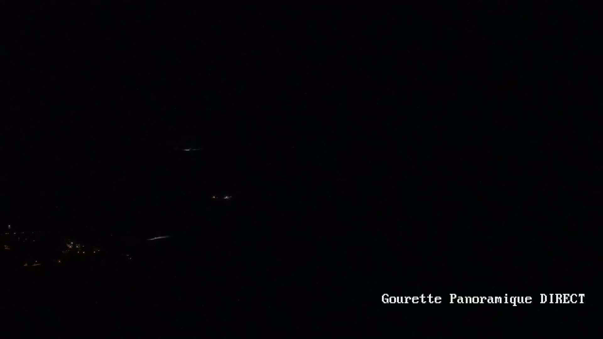 A dark nighttime scene shows a few distant lights on a landscape below.