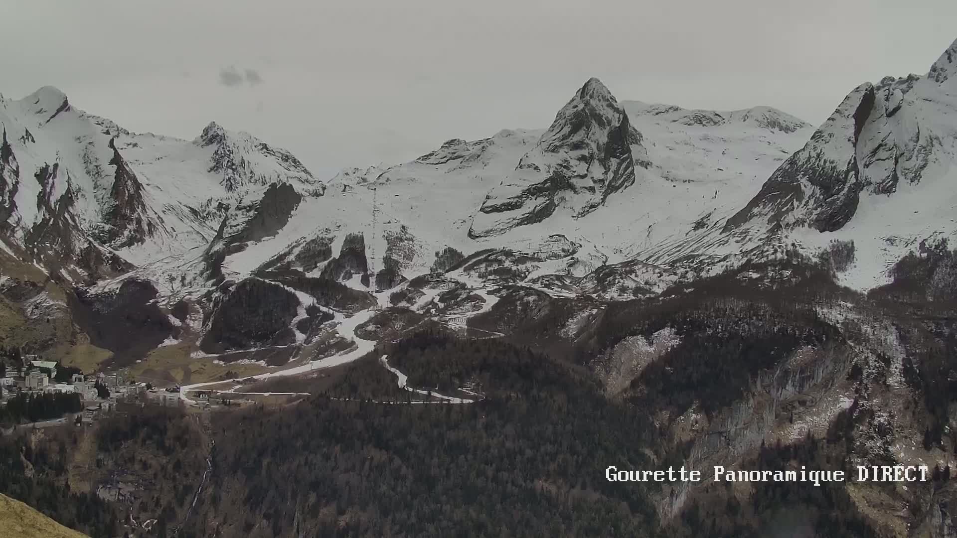 A long view shows a snow-covered mountain range under an overcast sky, with a town nestled in the valley below.