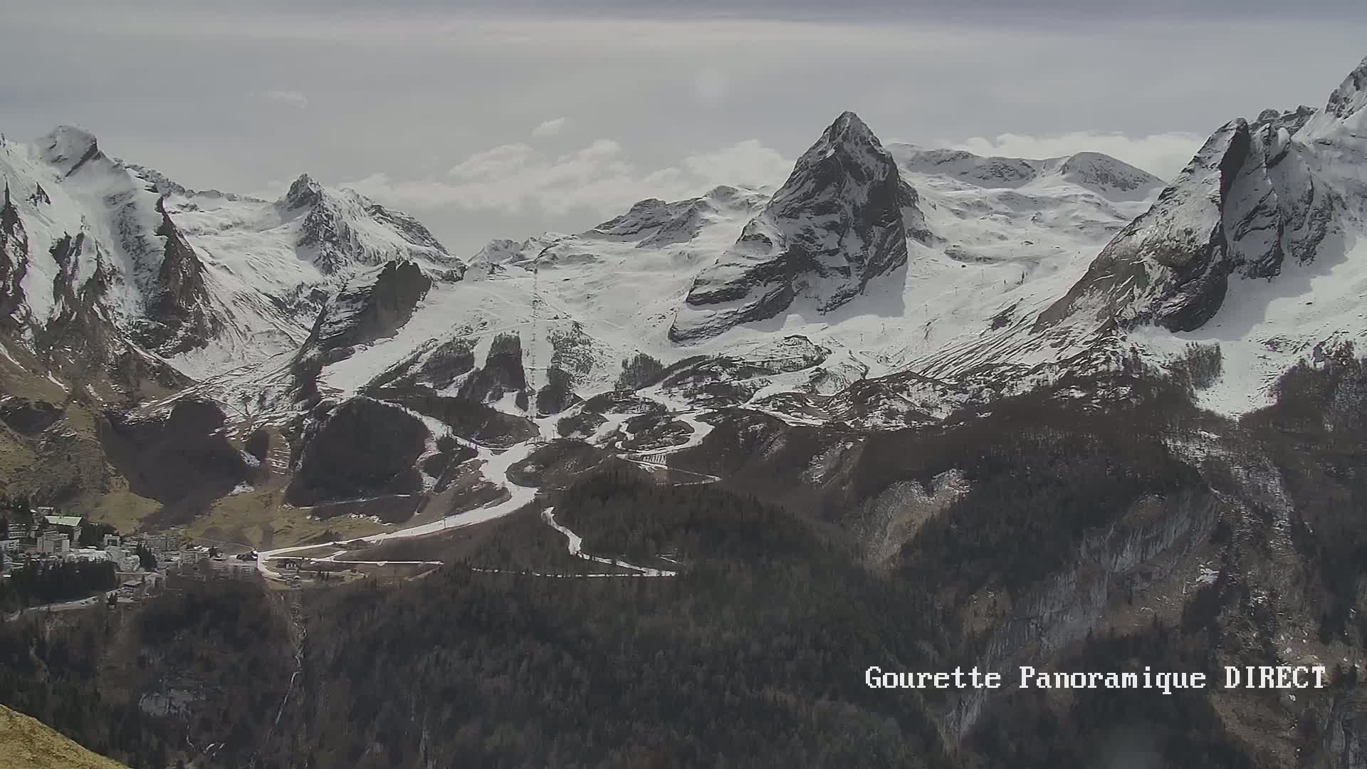 A snow-covered mountain range with a small town nestled below, under a cloudy sky.
