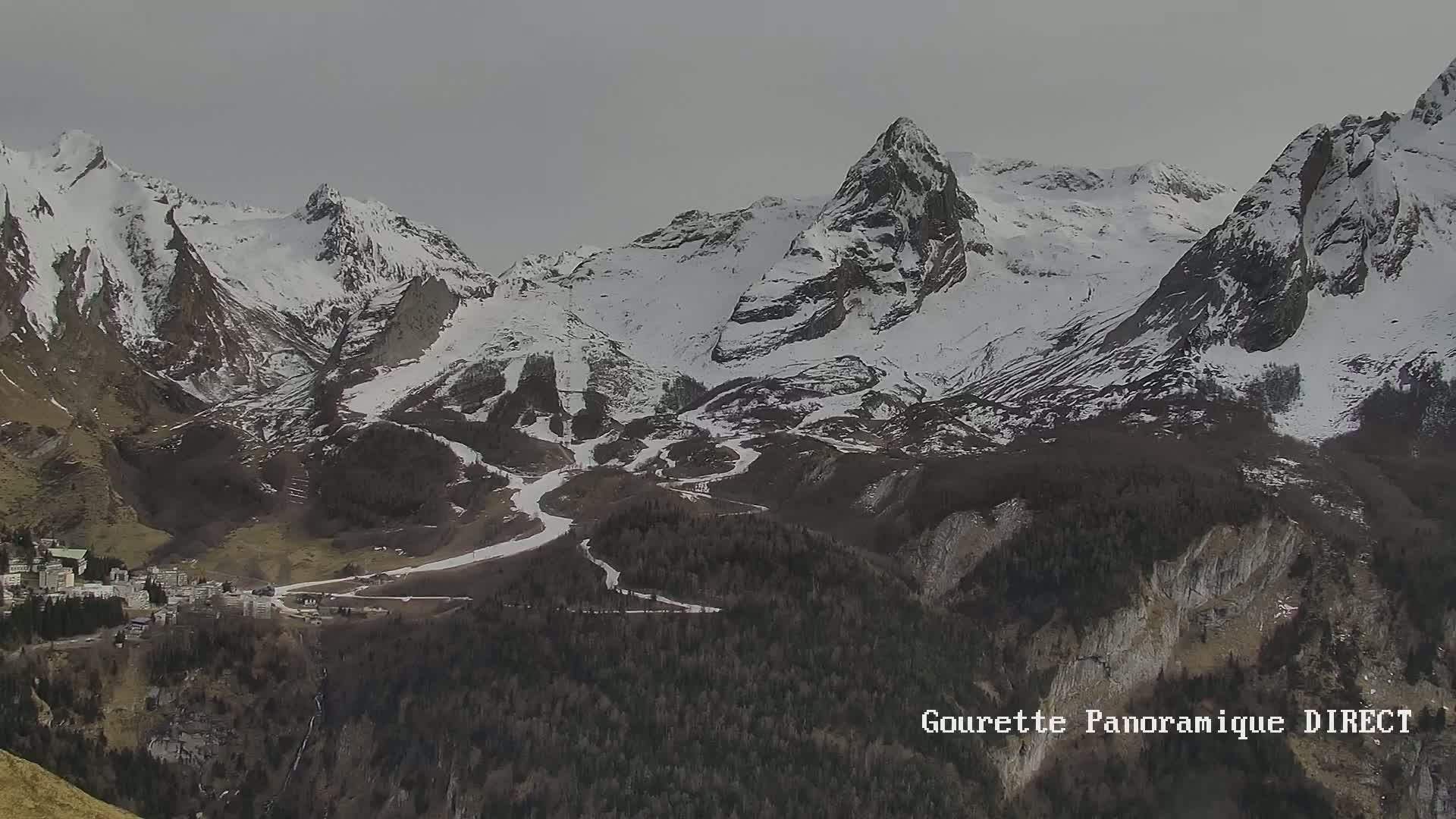 A snow-covered mountain range with a small town nestled in the valley below under an overcast sky.