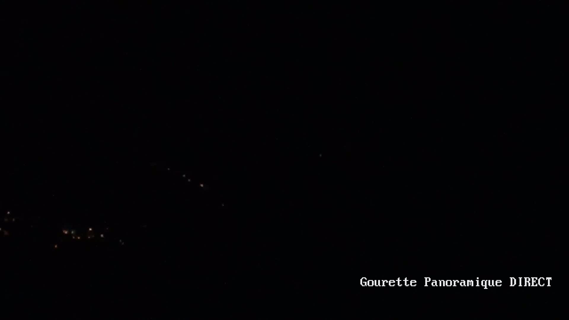 A nighttime long shot shows a scattering of faint, distant lights along a dark horizon.
