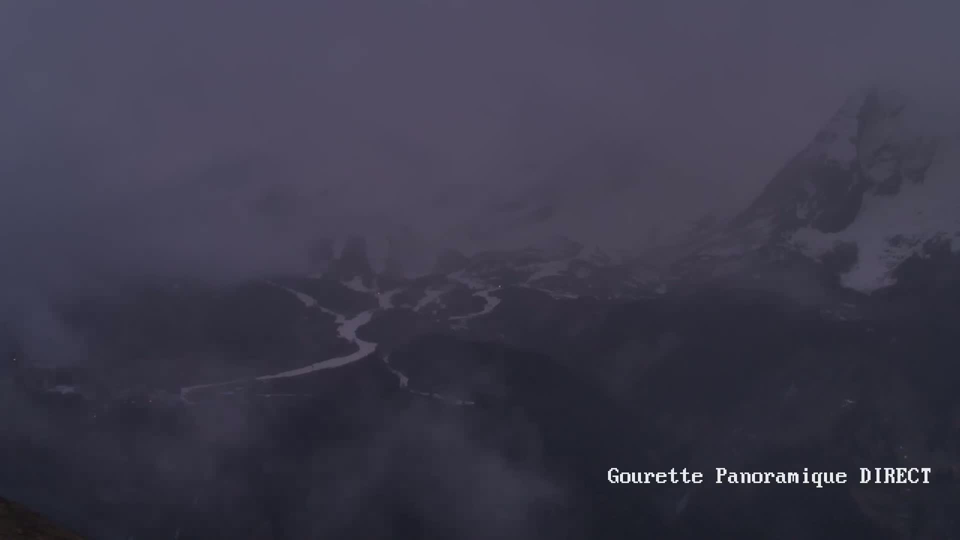 A misty, dark view of a snow-covered mountain range and valley.