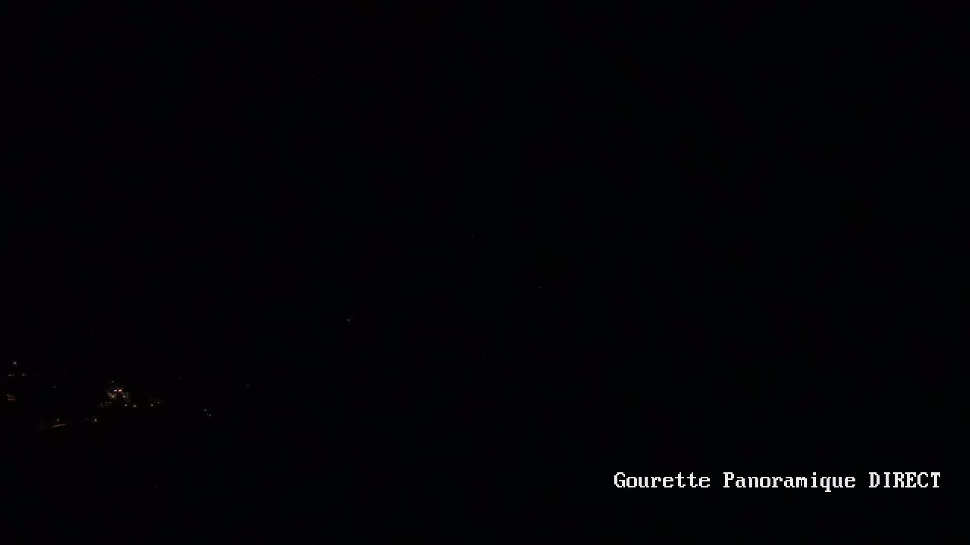 A nighttime, long-range view shows a few faint lights in the distance against a completely dark sky.