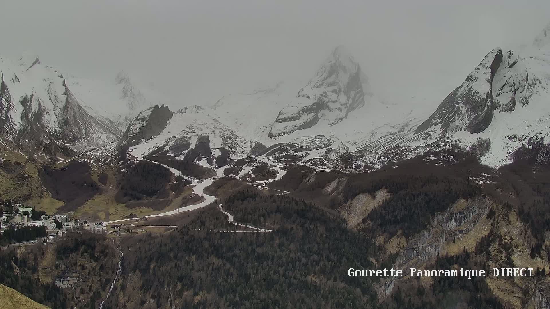 A snow-covered mountain range with a valley containing a small town below, under an overcast sky.