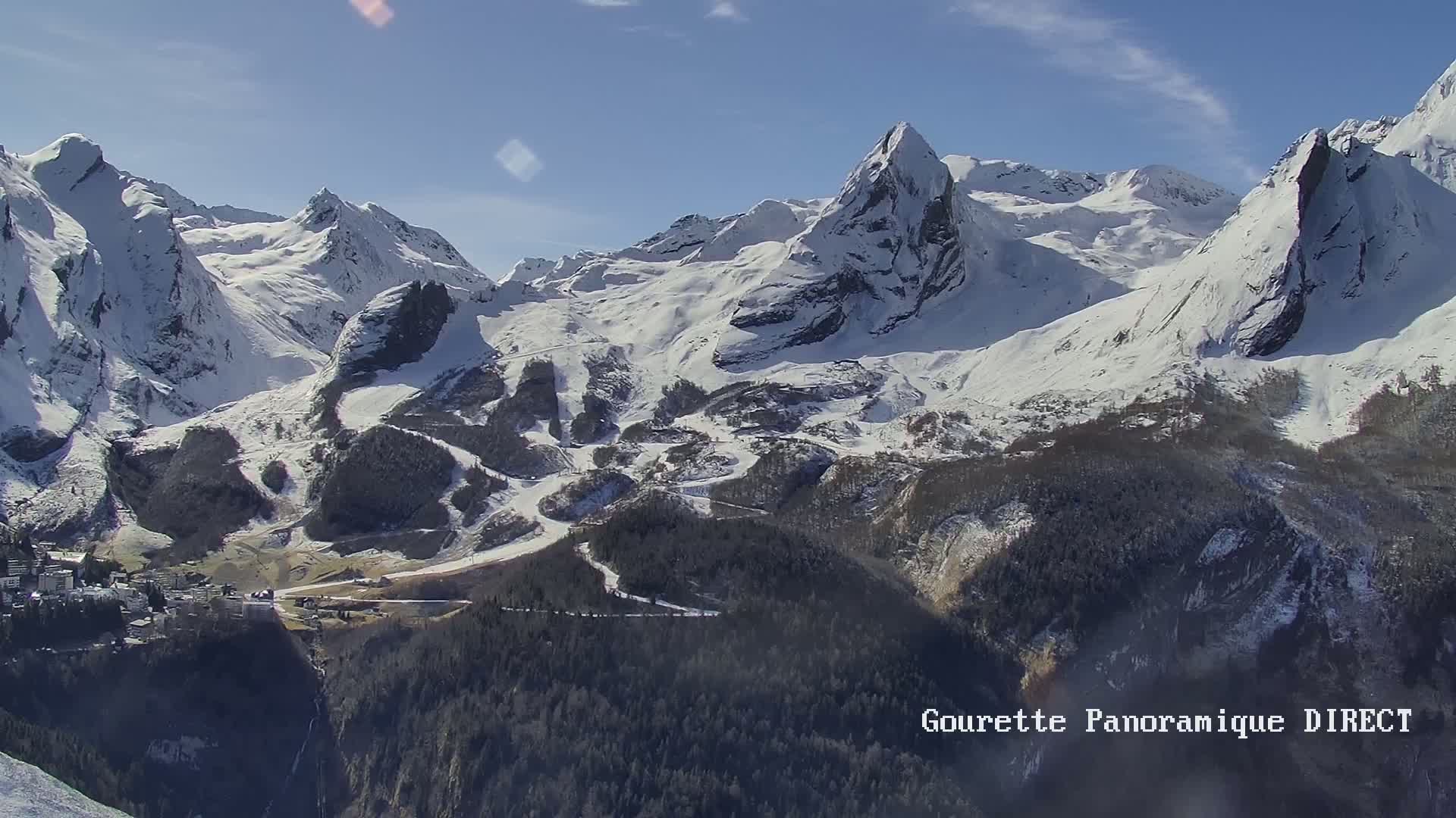 A snow-covered mountain range with a small town nestled in the valley below under a sunny sky.