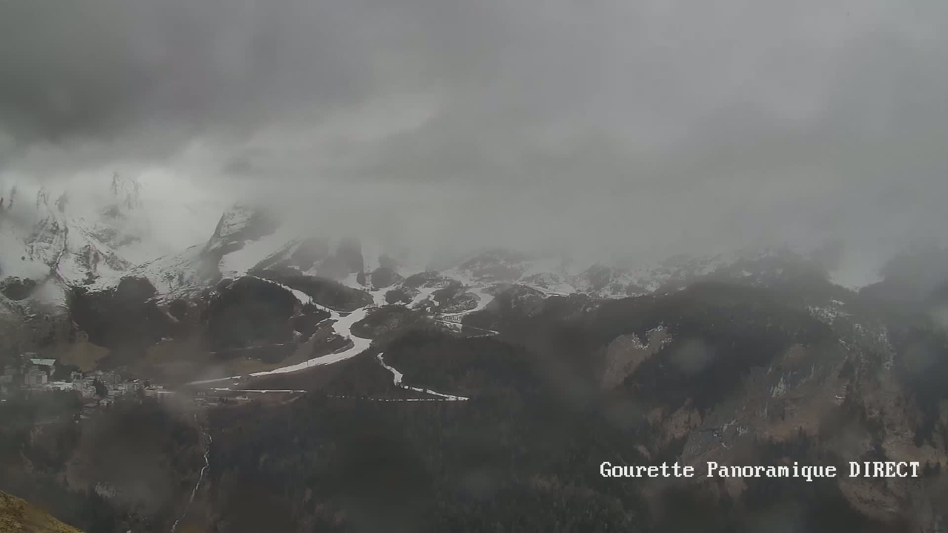 A snow-covered mountain range is shrouded in heavy fog and light snow.