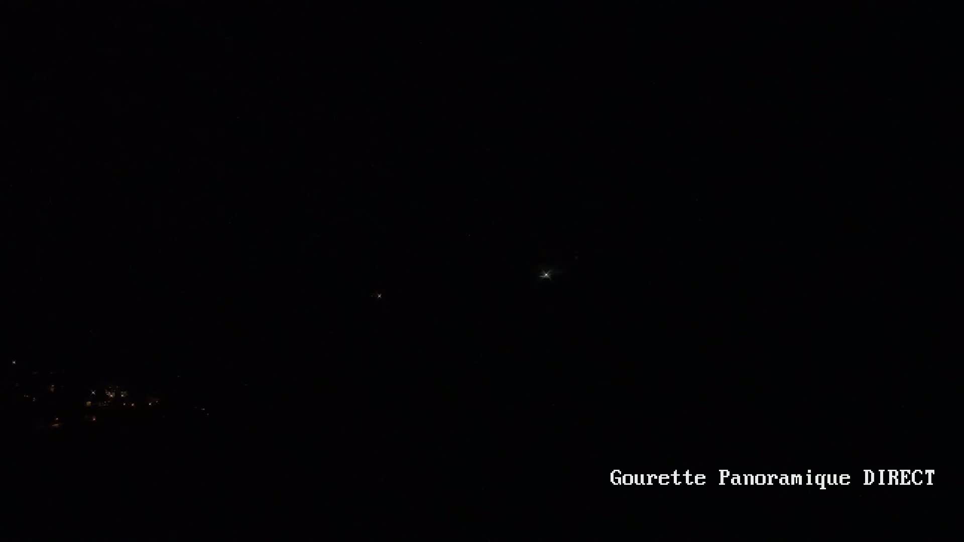 A dark night sky shows a few bright stars and distant lights below the horizon.