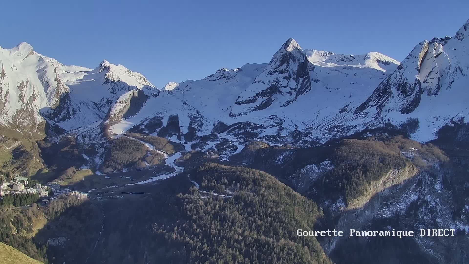A snow-covered mountain range with a small town nestled in the valley below on a clear, sunny day.