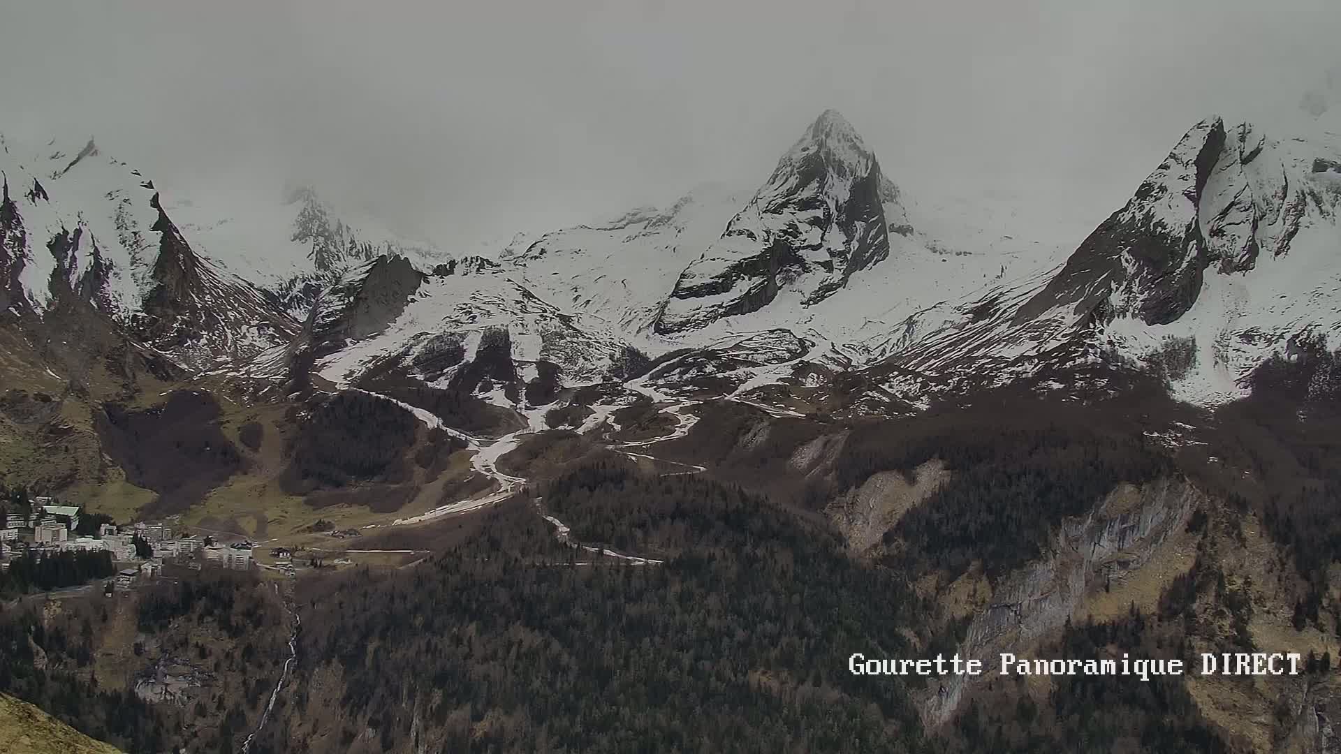 A valley town nestled beneath snow-capped mountains in overcast conditions.