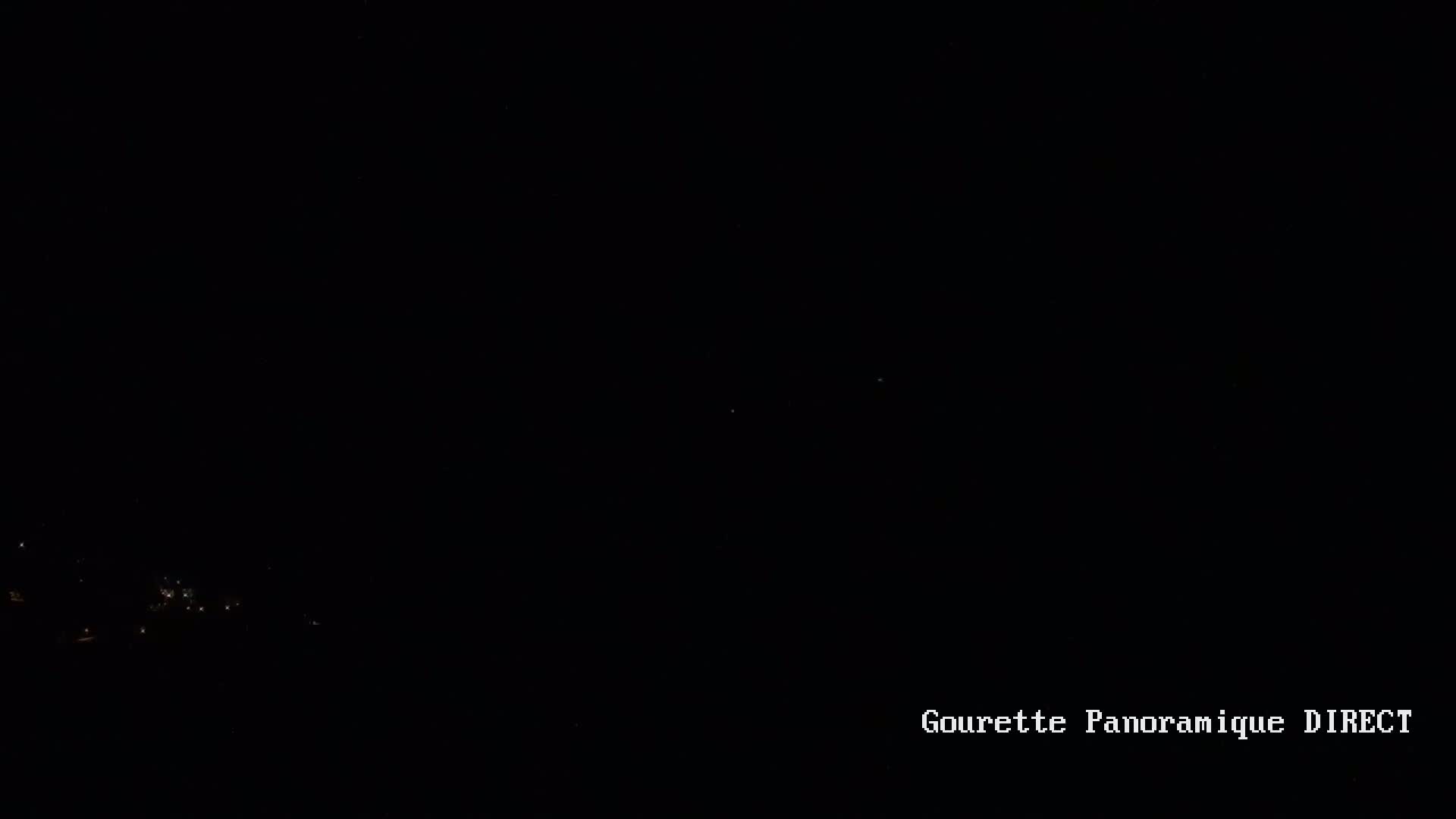 A nighttime long shot shows a few faint lights in the distance below a dark sky.