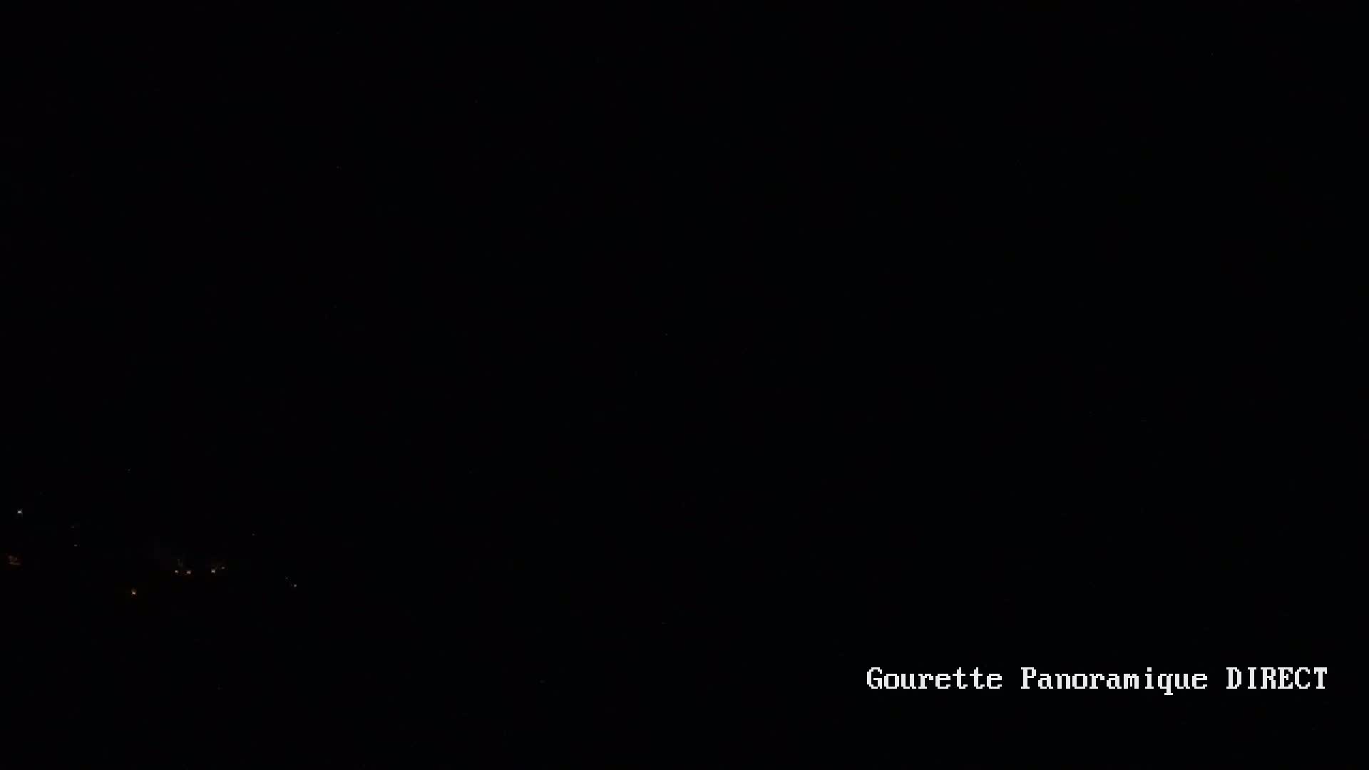 A nighttime, dark landscape shows a few faint lights in the distance.