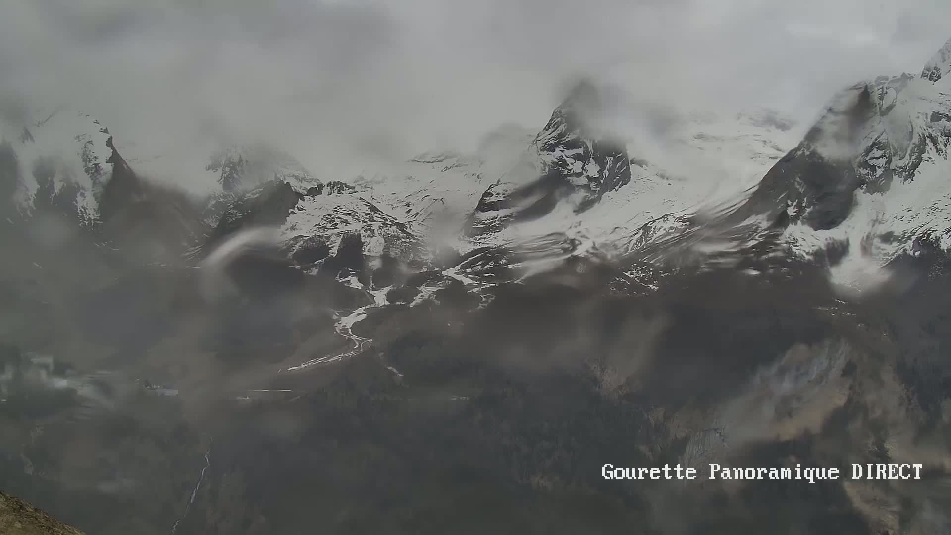 A misty, overcast view shows snow-capped mountains and valleys partially obscured by fog.