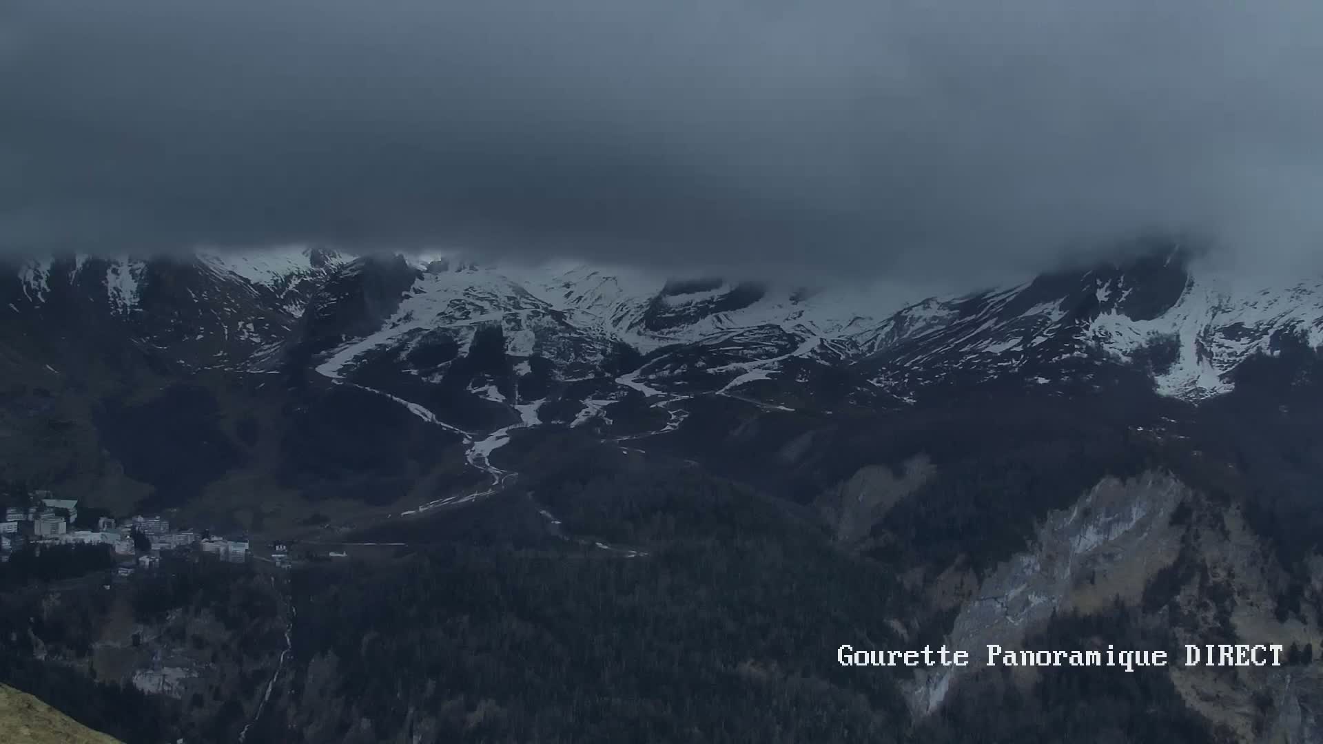A snow-capped mountain range is mostly obscured by a low-hanging cloud cover.