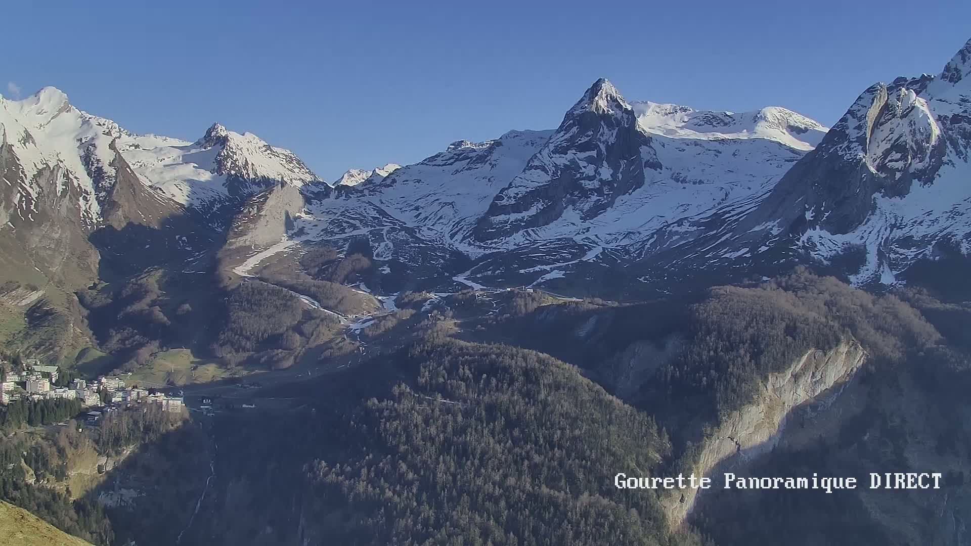 A snow-capped mountain range is visible under a clear blue sky, with a town nestled in the valley below.
