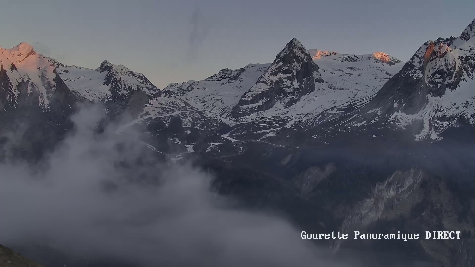 A snow-capped mountain range is partially obscured by low-lying clouds at dawn.