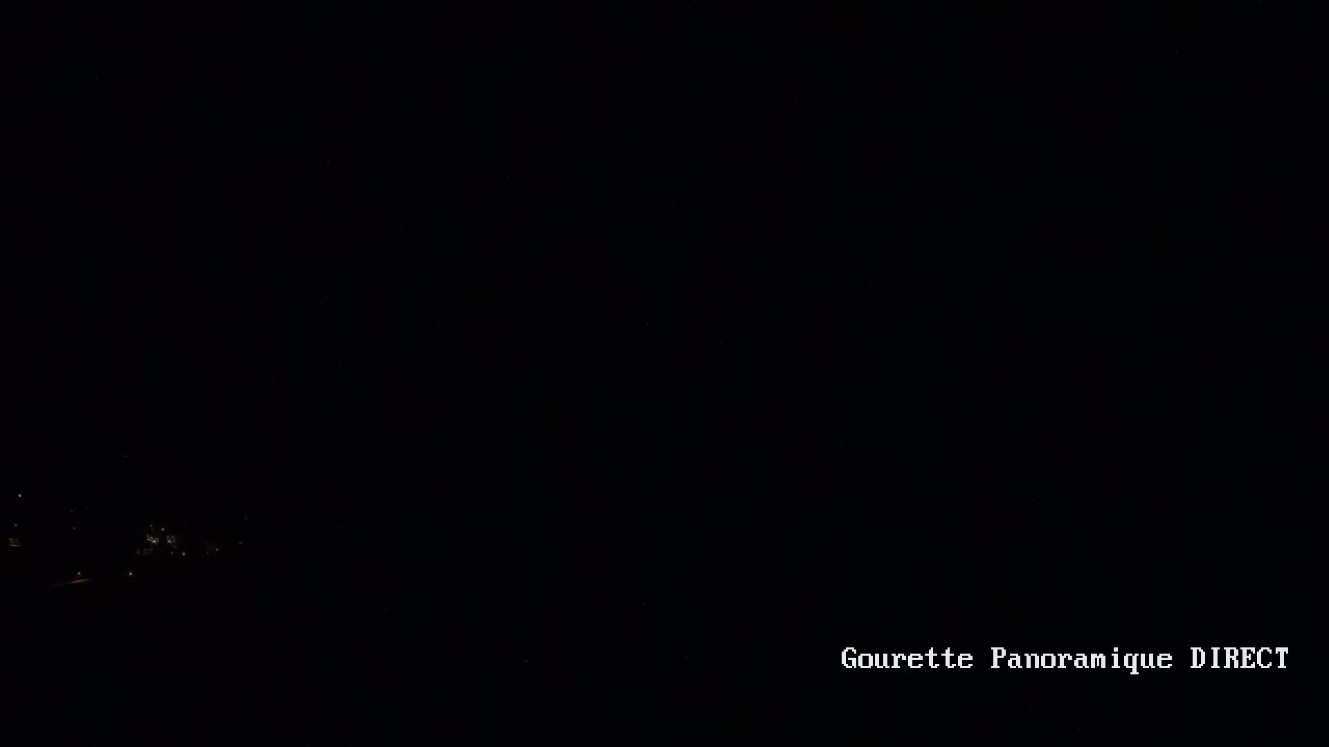 A nighttime view shows a few distant, faint lights at the bottom of the frame, under a dark, clear sky.